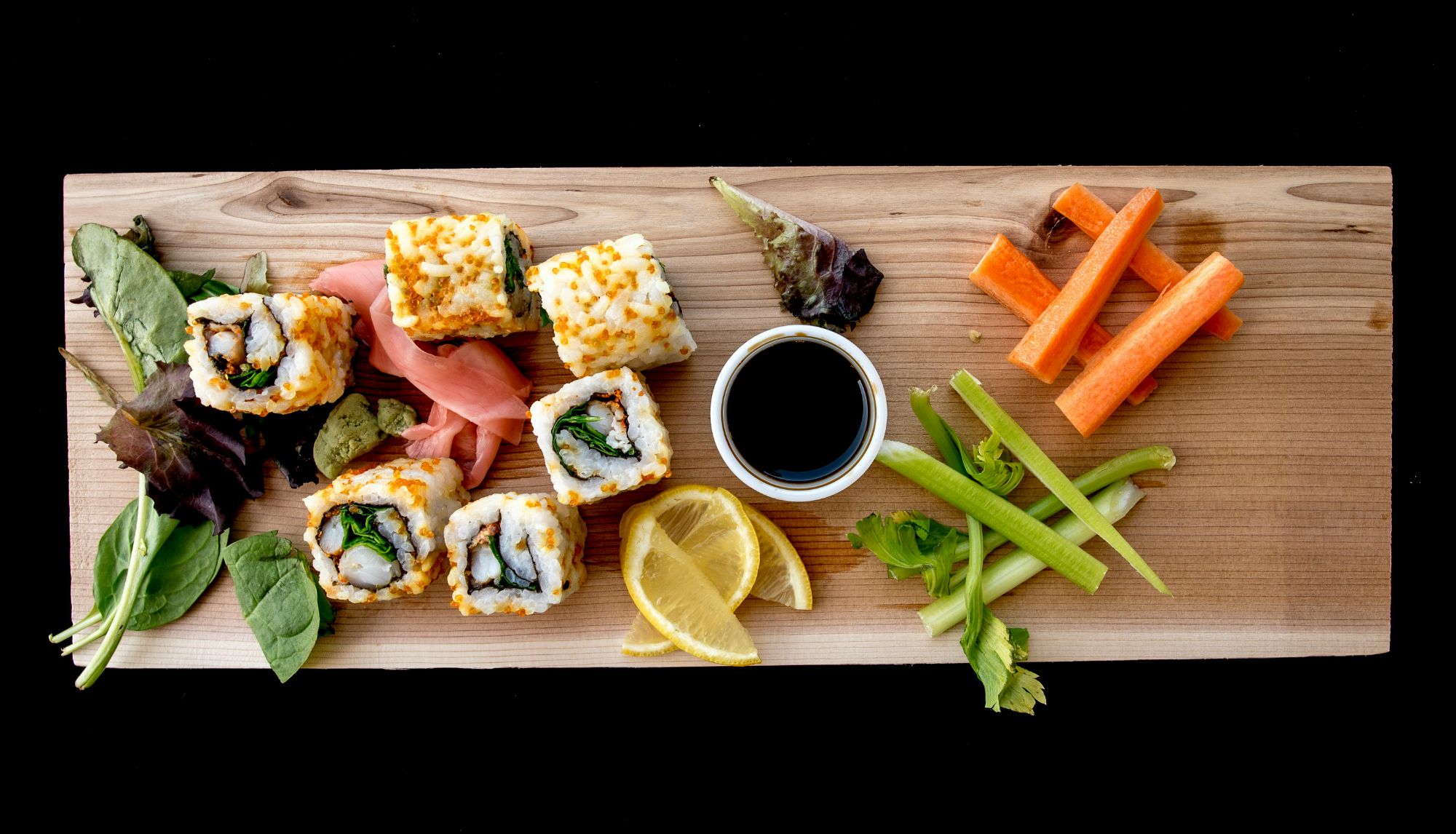 Sushi na desce: rolki, wasabi, plasterki cytryny, warzywa i sos sojowy.