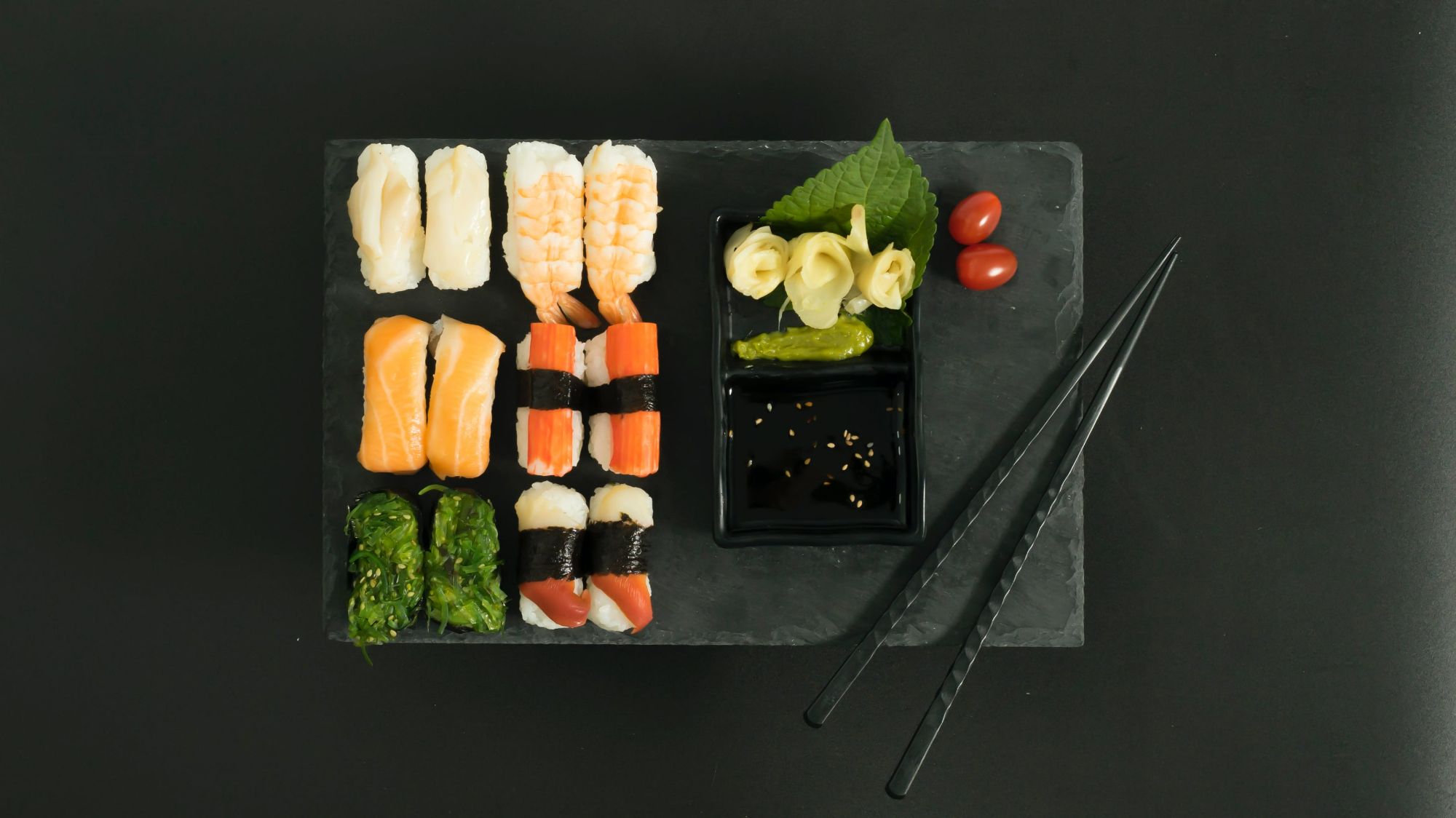 Taca z sushi: różne kawałki sushi, sos sojowy, wasabi, marynowany imbir i chopsticki.