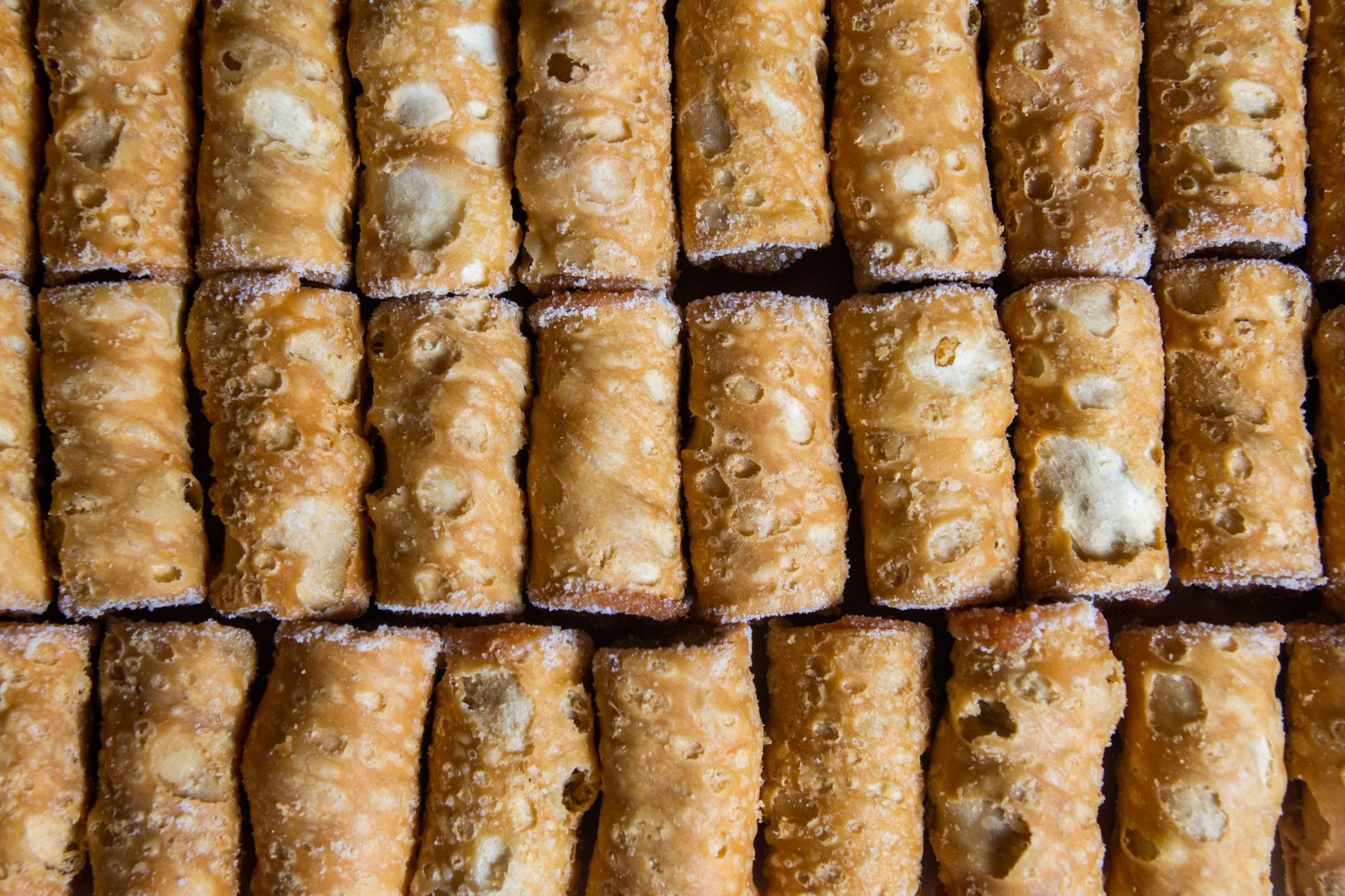 Równomiernie ułożone rurki ciastkowe posypane cukrem pudrem, z różnorodnymi nadzieniami.