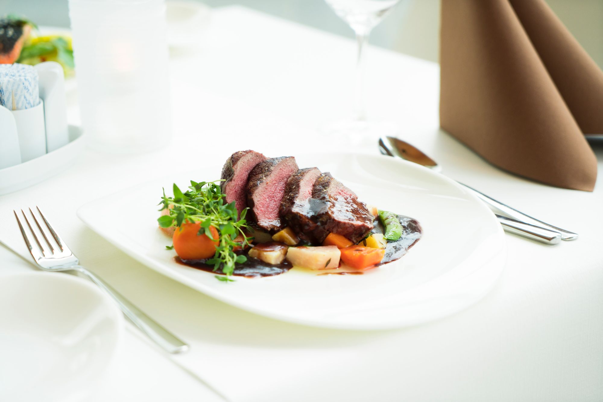 Smażona wołowina z sosem, warzywami i ziołami na białym talerzu w eleganckiej restauracji.