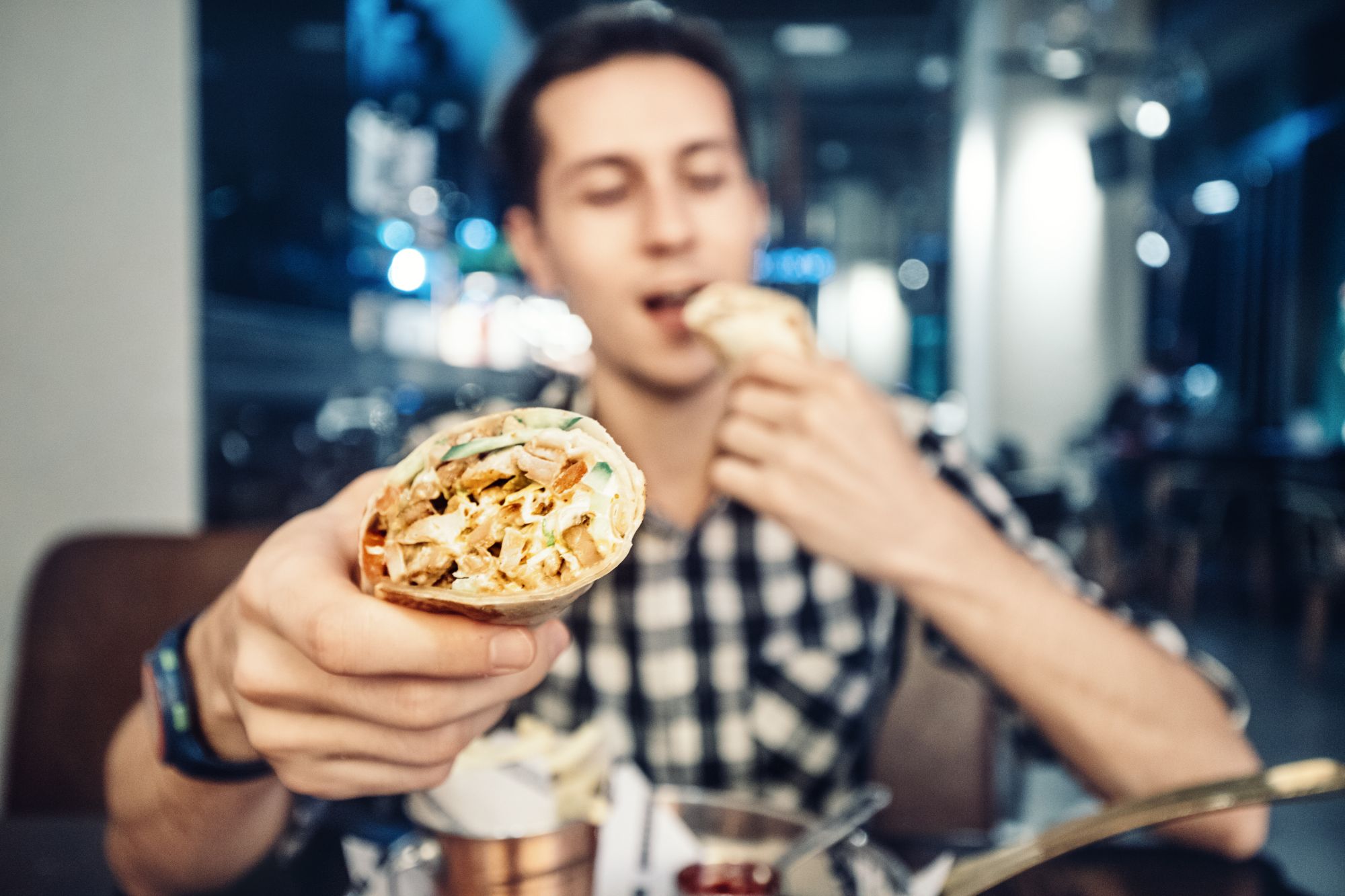 Mężczyzna w koszulce w kratę trzyma w ręku burrito, siedząc w restauracji.