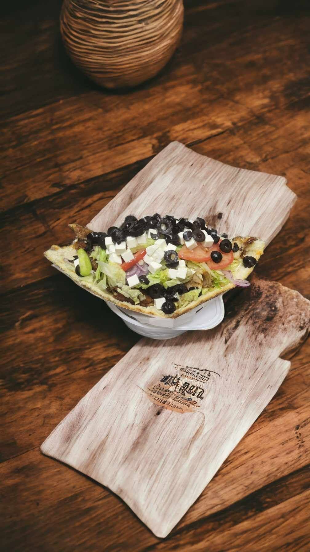 Taco z sałatką, czarnymi fasolami i serem feta na drewnianym talerzu.