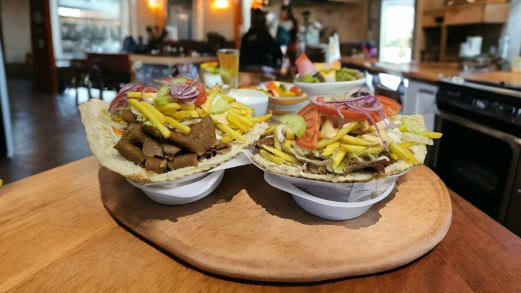 Oba talerze z kanapkami, mięsem, frytkami i warzywami, ustawione na drewnianym stole w restauracji.