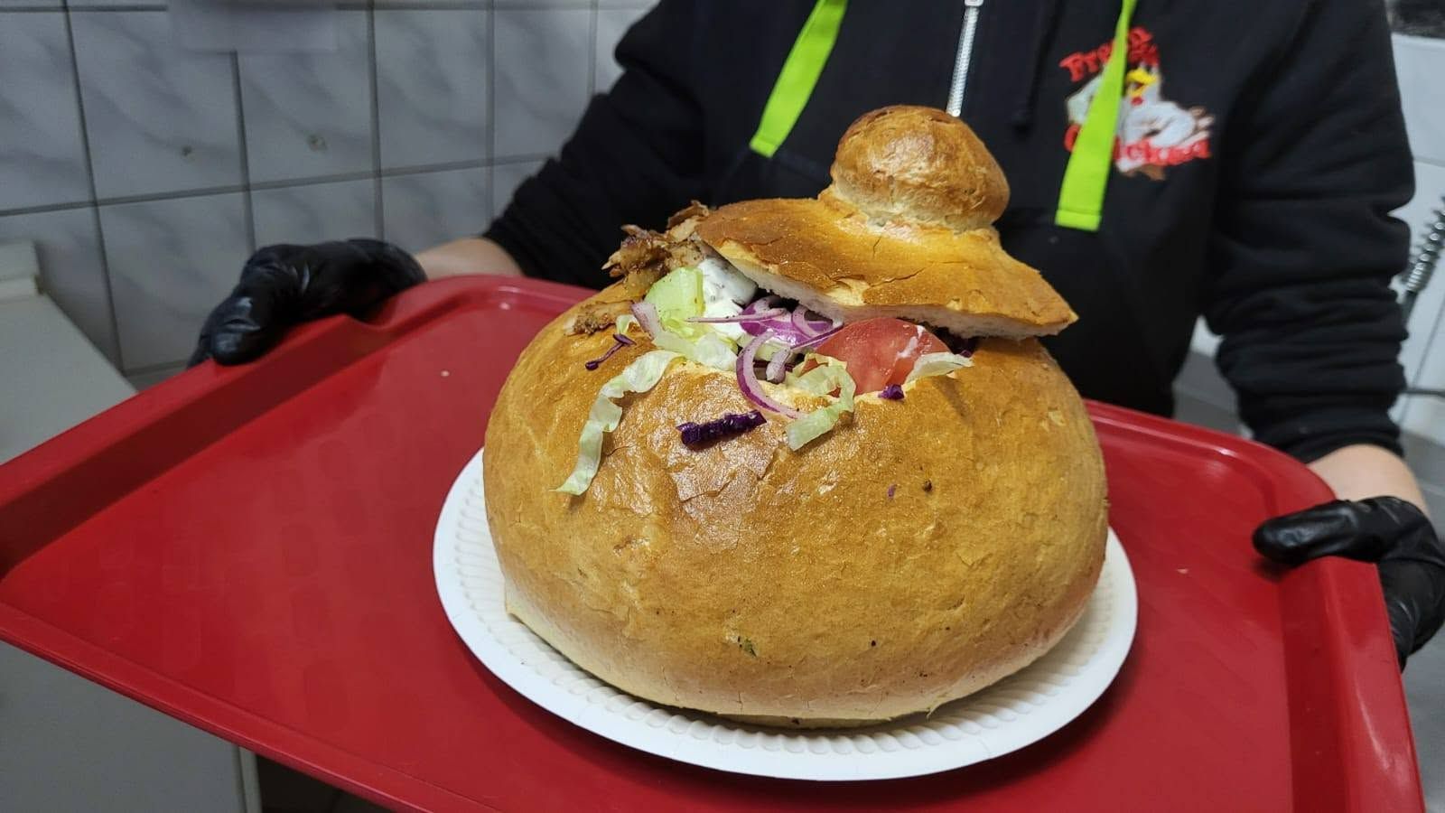 Pyszny chlebek z farszem, sałatą i warzywami, podawany na talerzu przez osobę w rękawiczkach.