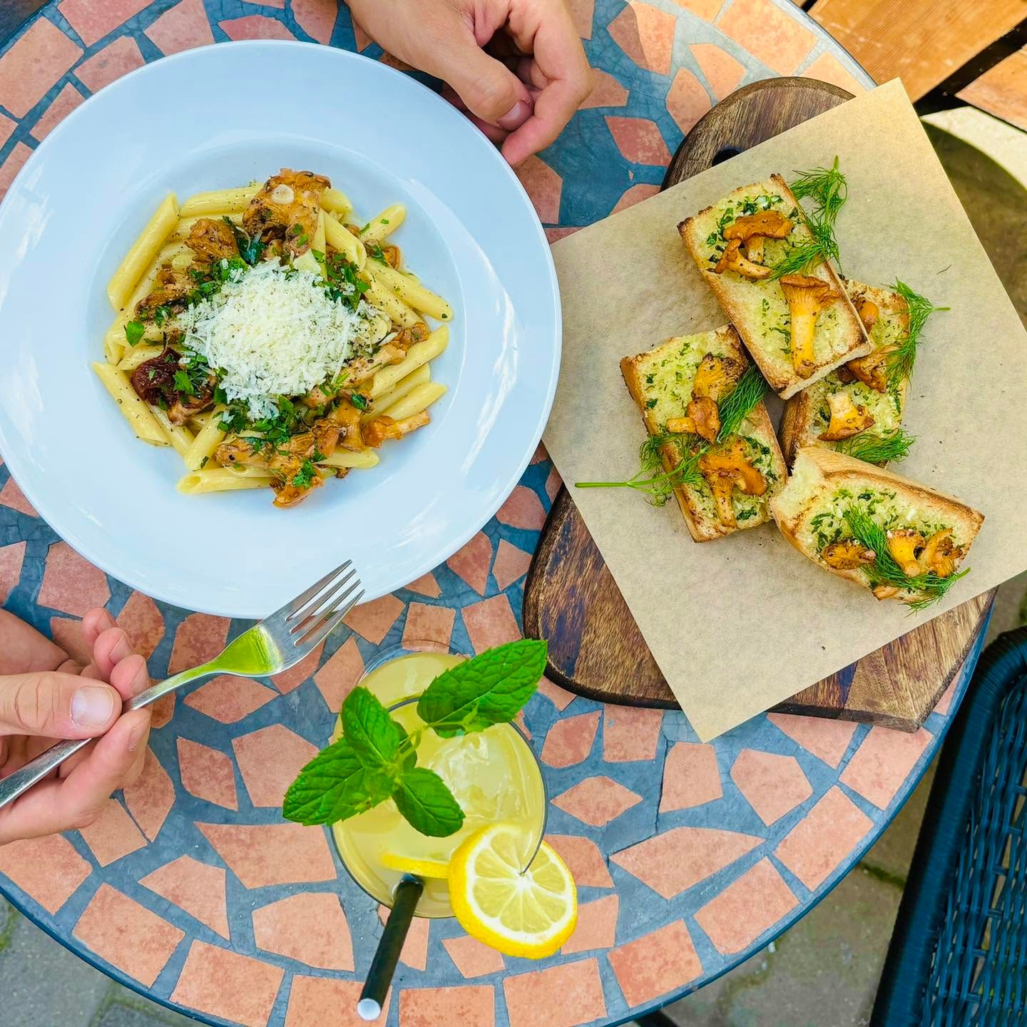 Spaghetti z sosem grzybowym, pieczywo czosnkowe i lemoniada na stole w kawiarnianym otoczeniu.