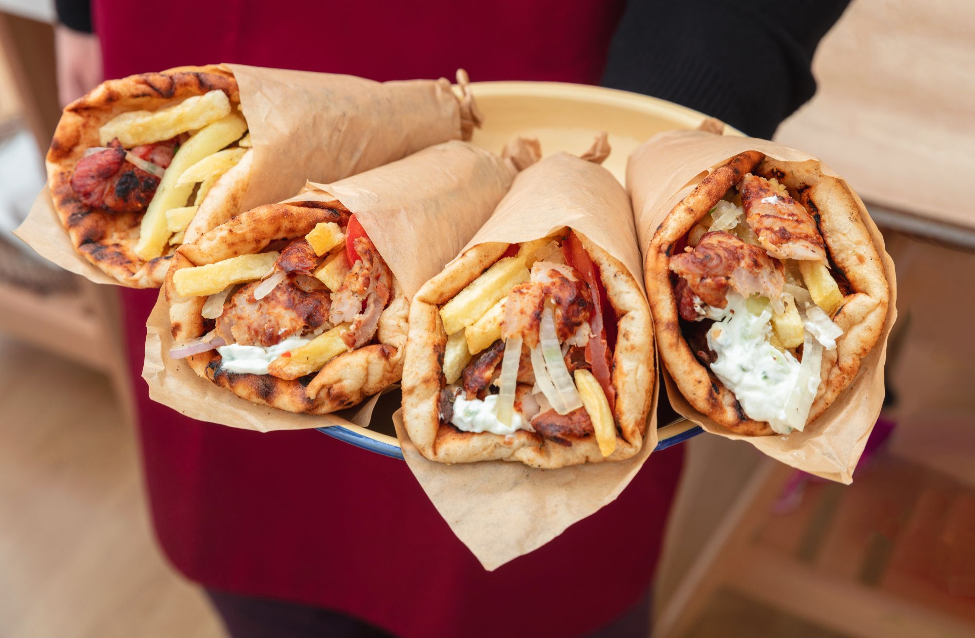 Talerz z czterema kebabami w tortilli z frytkami i sosem, podawany przez osobę.