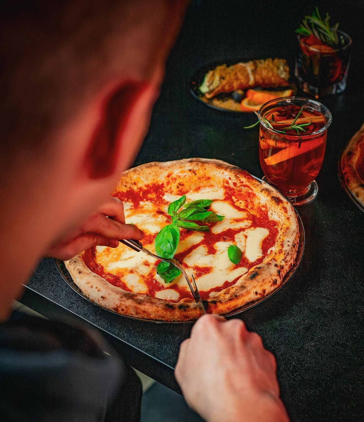 Osoba jedząca pizzę Margherita z bazylią i sosem pomidorowym przy stole z napojem.