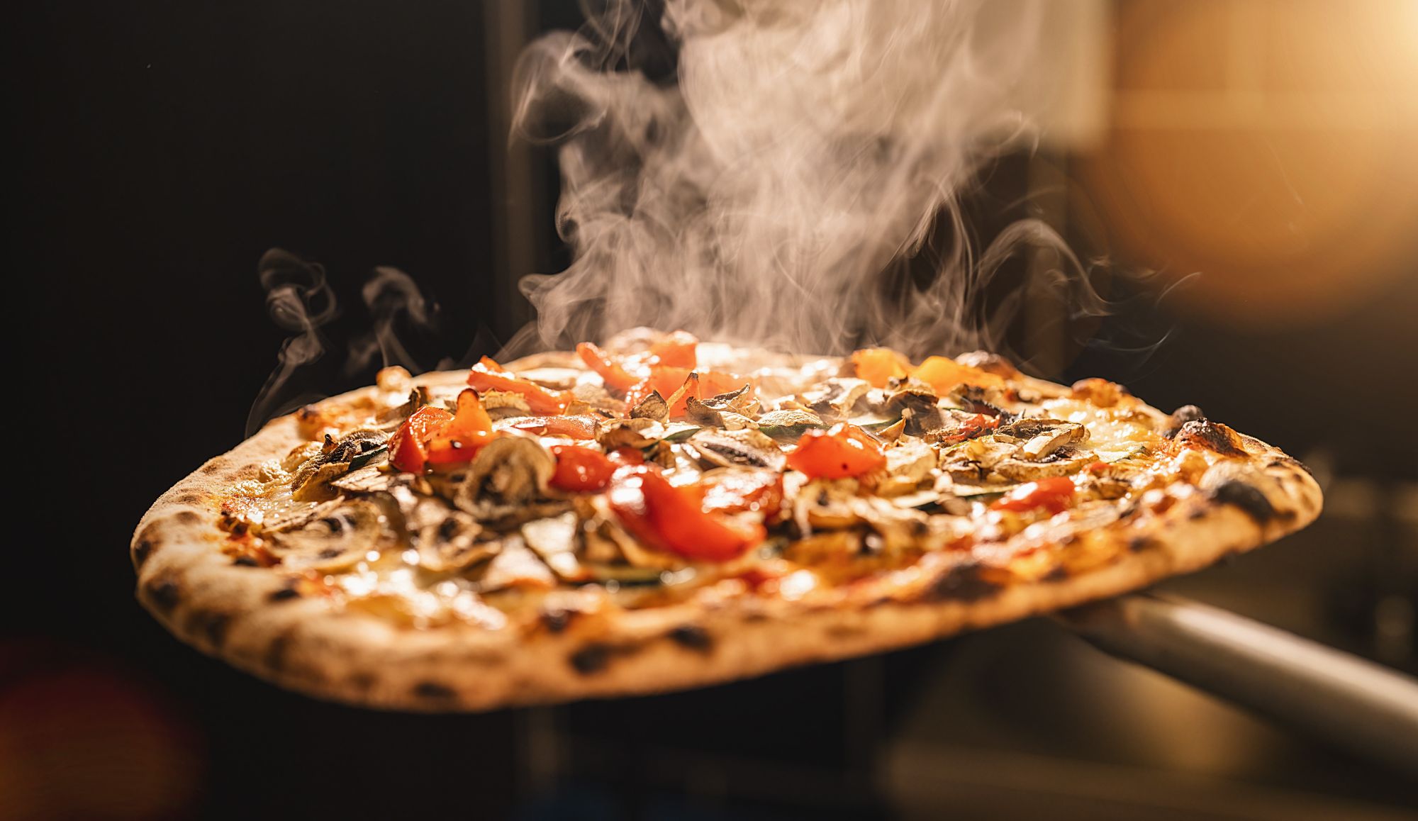 Pachnąca pizza z pomidorami, pieczarkami i ziołami, unosi się w powietrzu z wydobywającym się dymem.