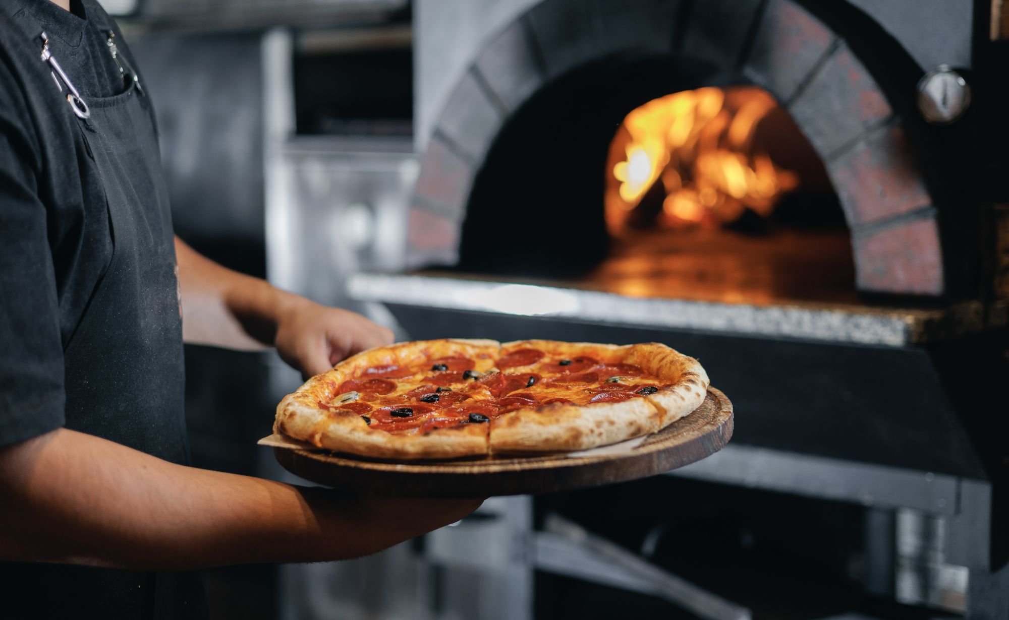 Piekarz podaje świeżą pizzę pepperoni z pieca opalanego drewnem.
