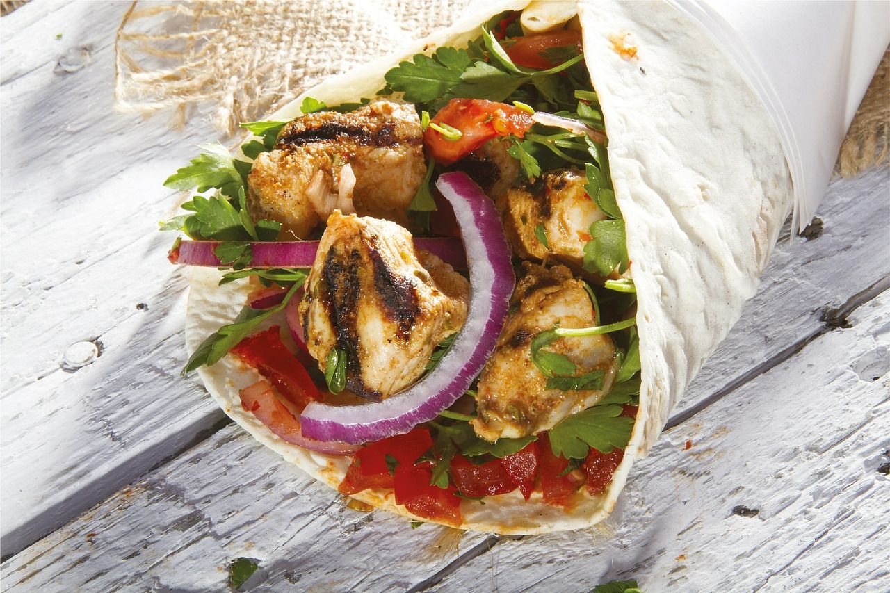 Wrap z grillowanym kurczakiem, warzywami, sosem, otoczony kawałkiem białego chleba, na drewnianym tle.