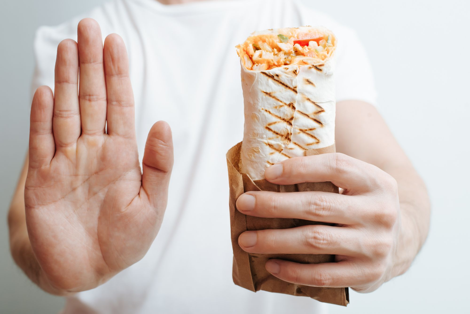 Osoba trzymająca burrito w papierowej torebce, z uniesioną dłonią w geście "stop".