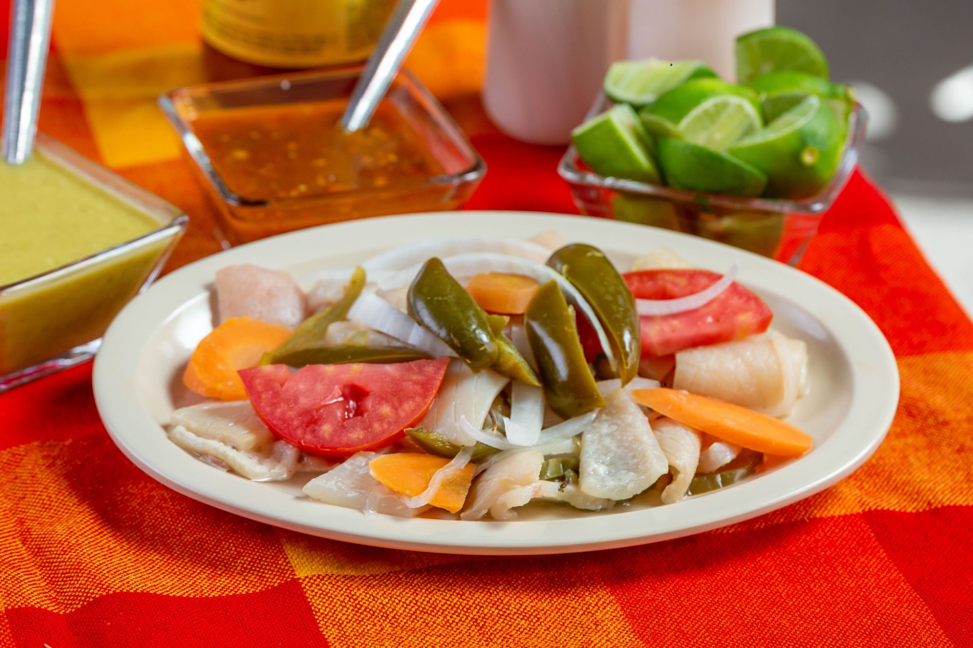 Talerz z marynowanym warzywami: cebula, papryka, pomidor, marchewka, podany z limonkami i sosem.