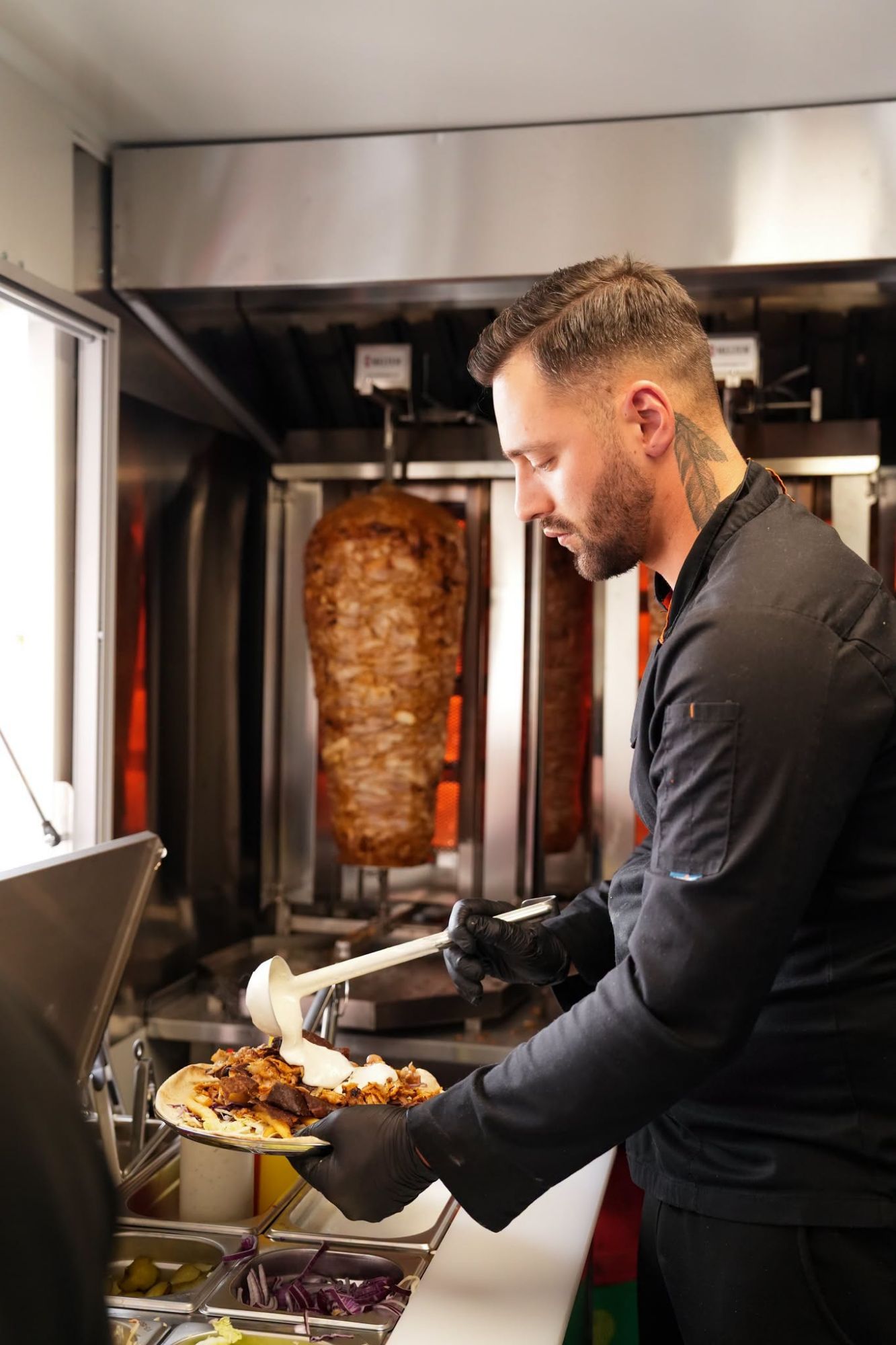 Kucharz w czarnym fartuchu nakłada jedzenie na talerz w food trucku z kebabem.