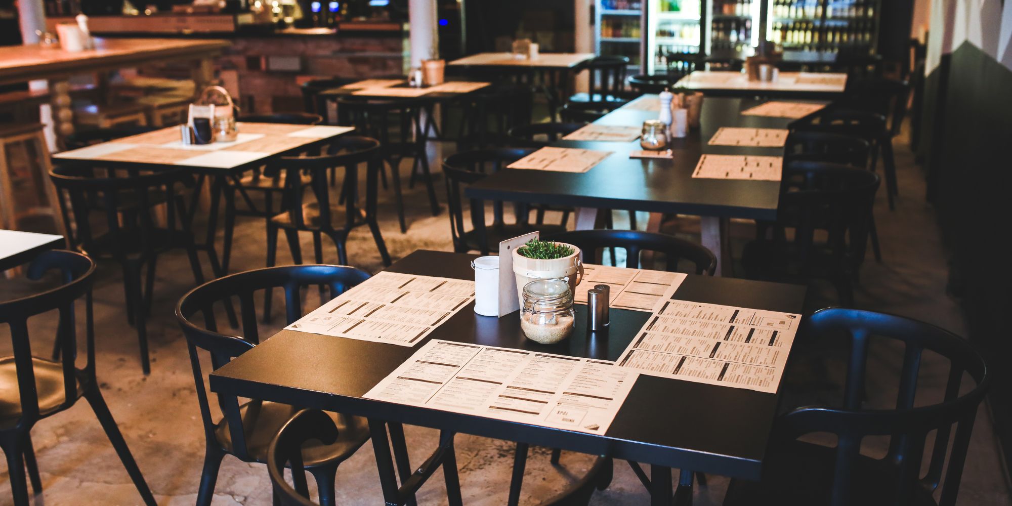 Wnętrze restauracji z czarnymi stołami, menu na stole i przytulną atmosferą.
