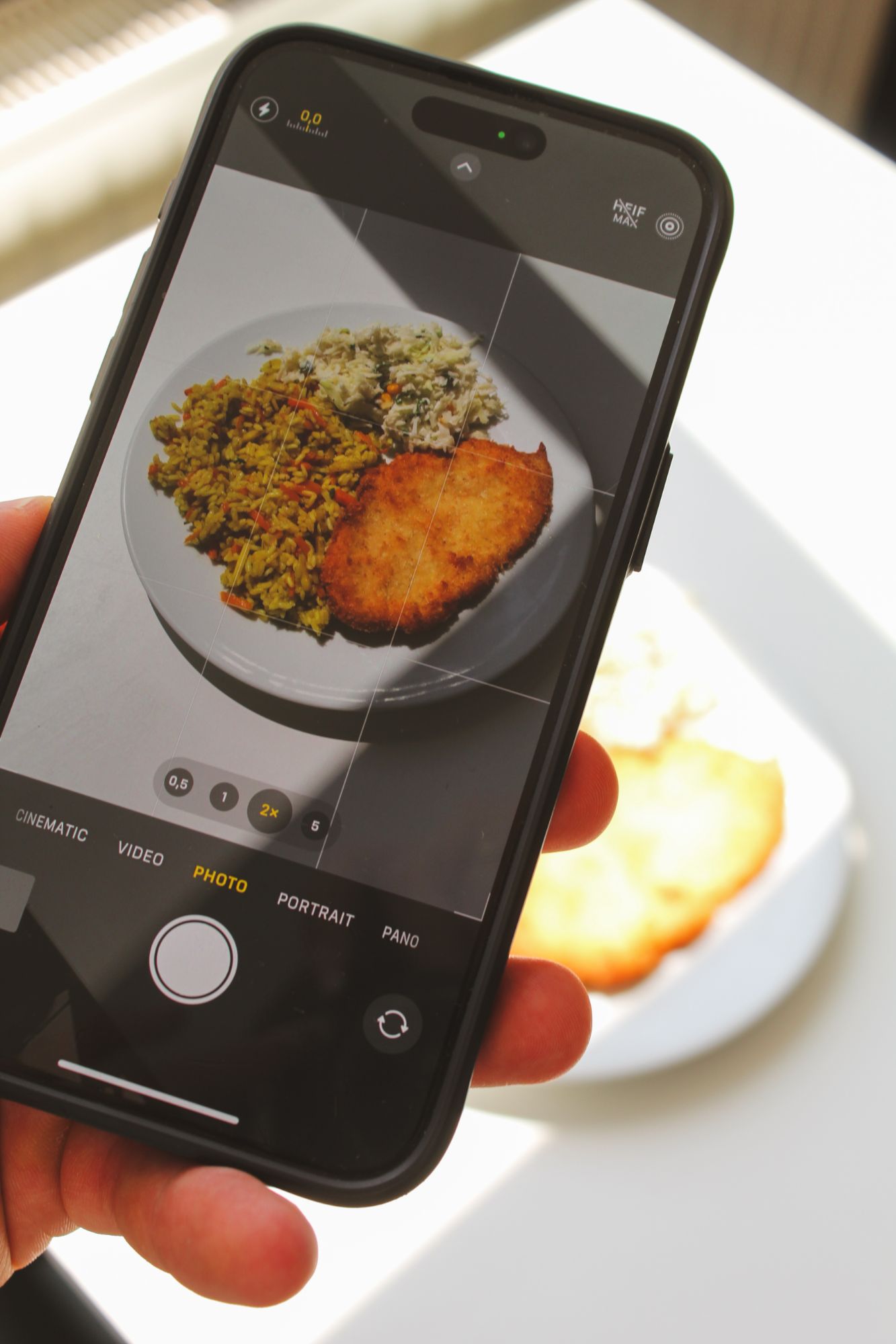 Osoba trzymająca telefon, fotografująca talerz z ryżem i kotletem na jasnym tle.