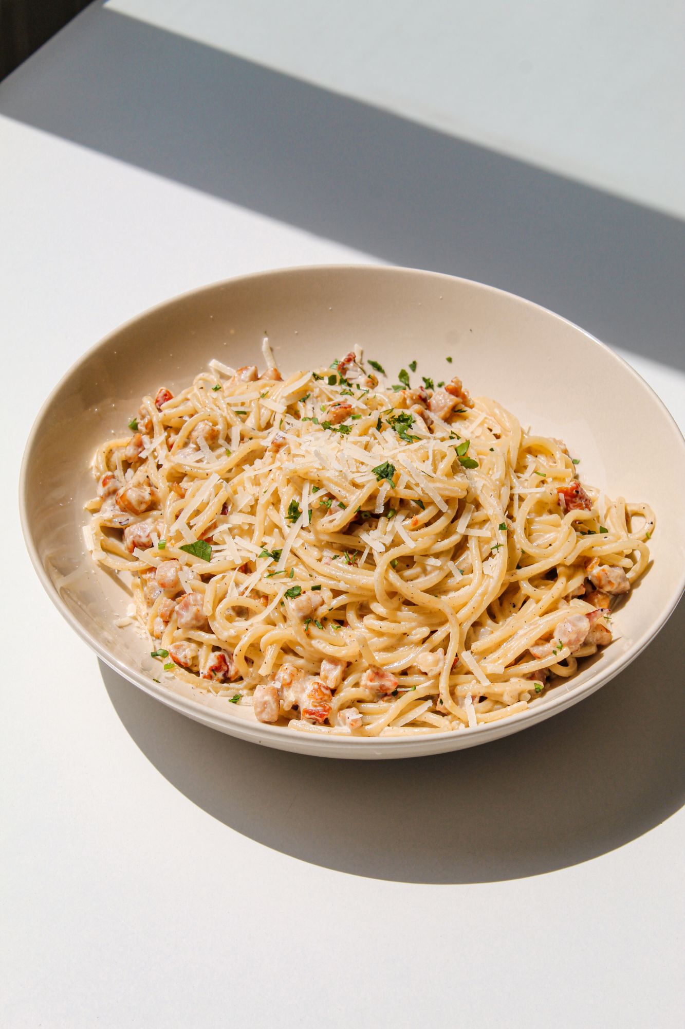 Talerz spaghetti z sosem, posypany serem i ziołami, na jasnym tle.