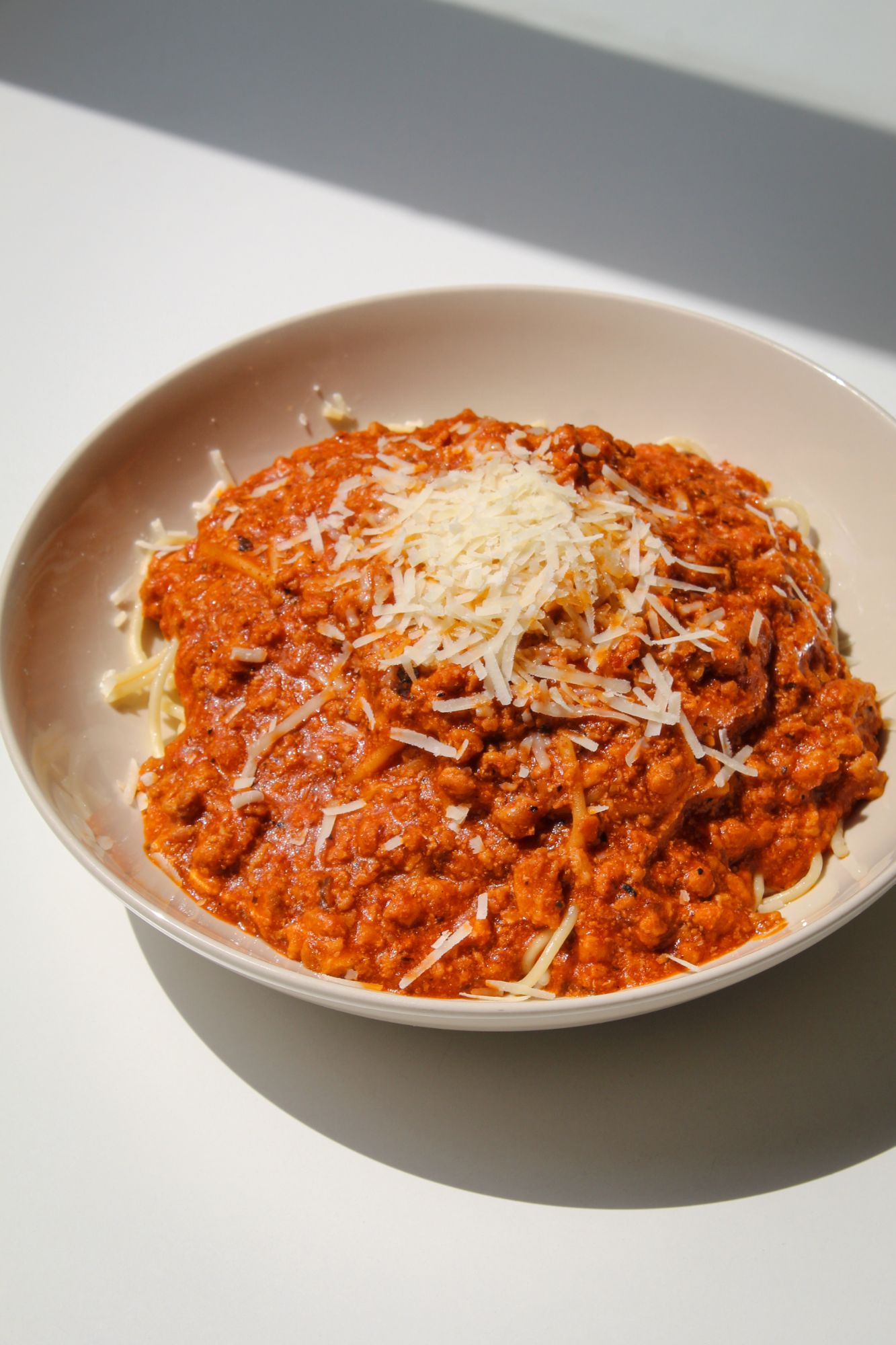 Makaron spaghetti z sosem bolognese i startym serem na jasnym tle.