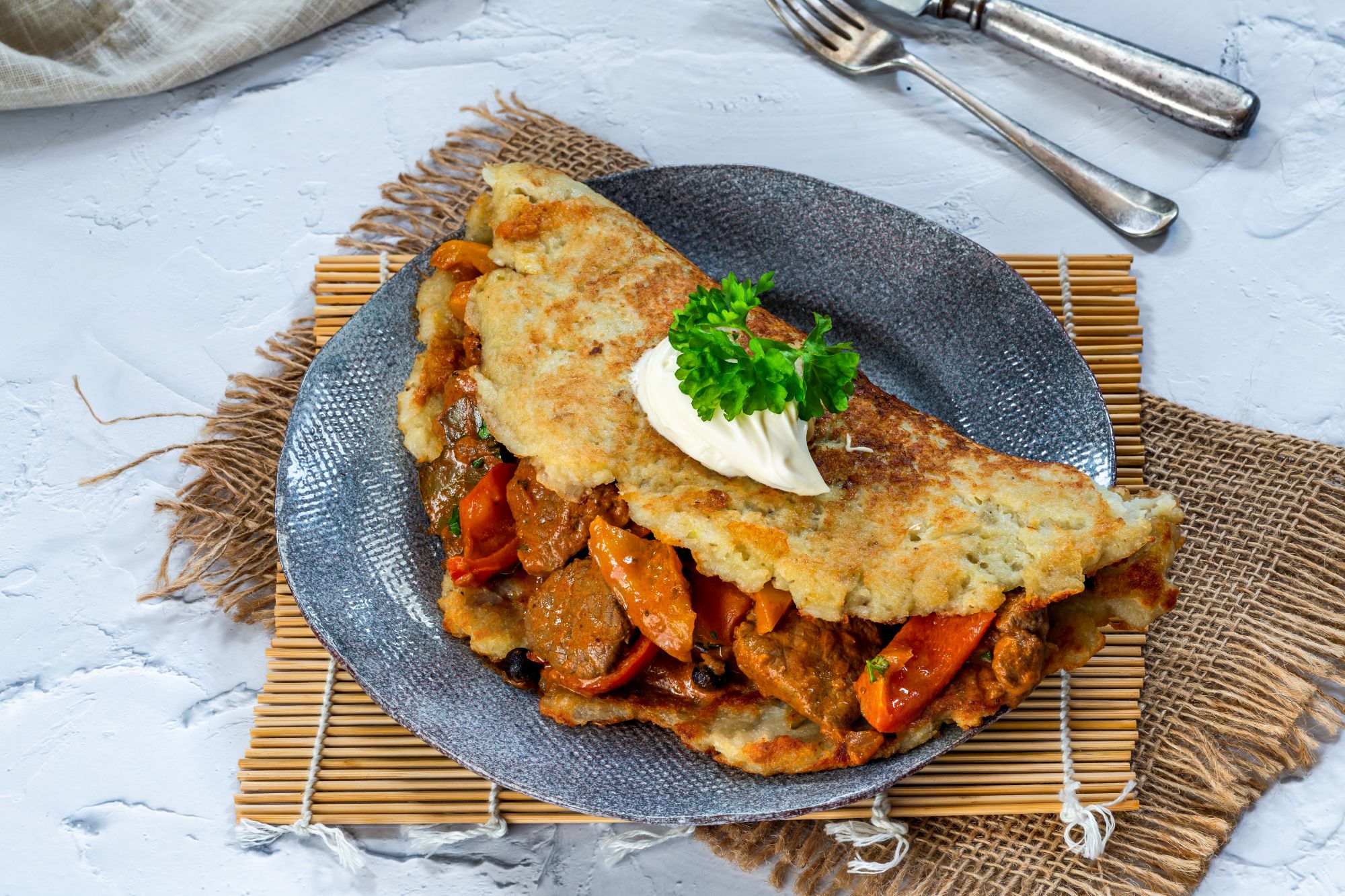 Omlet z mięsem i warzywami, podany z kleksem śmietany, na talerzu, na tle naturalnych materiałów.