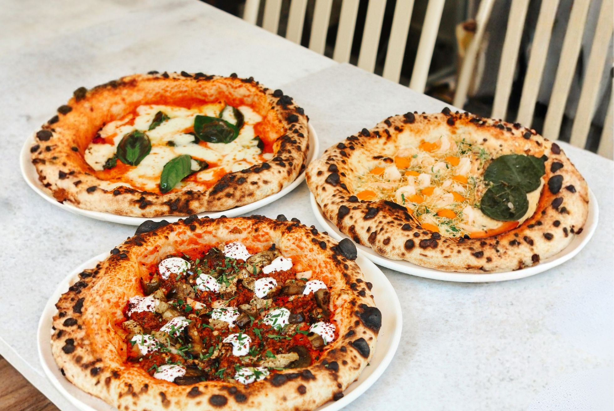 Trzy różne pizze na białych talerzach: margherita, z serem i szpinakiem oraz pizza z różnorodnymi dodatkami.