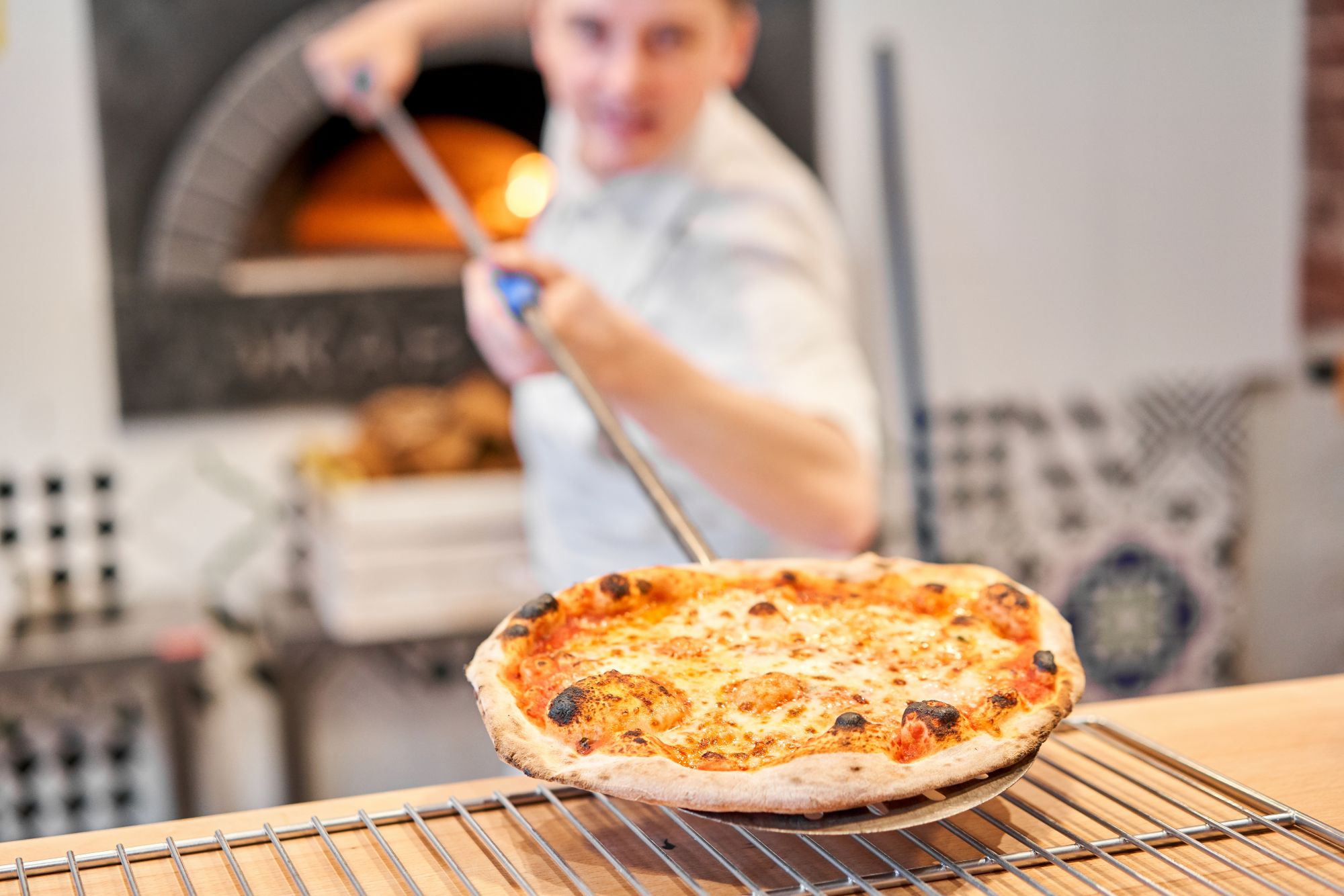 Pizzeria: kucharz wyciąga świeżo upieczoną pizzę z pieca opalanego drewnem.