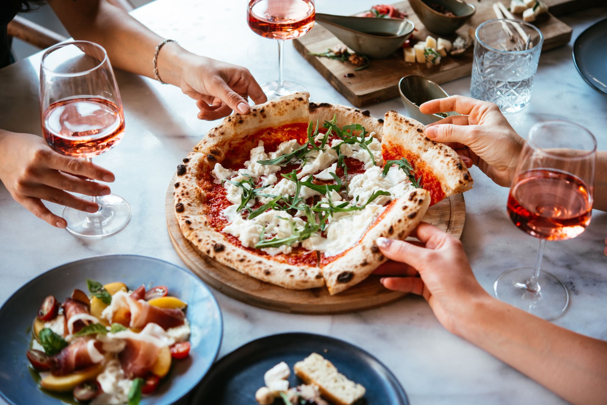 Osoby dzielą się pizzą z serem, świeżą bazylią i winem różowym w eleganckiej restauracji.