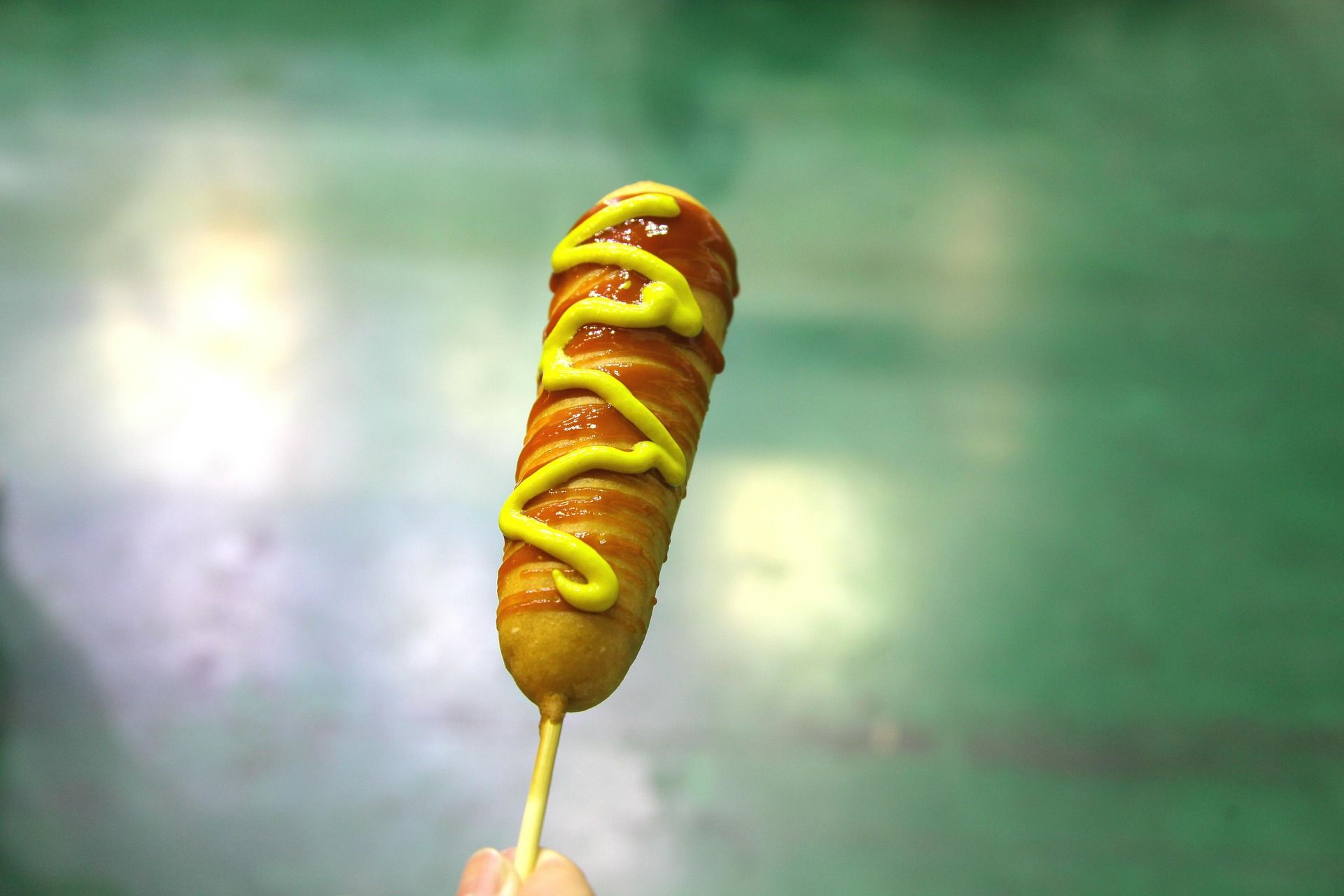 Kiełbasa na patyku z ketchupem i musztardą na tle zielonej podłogi.