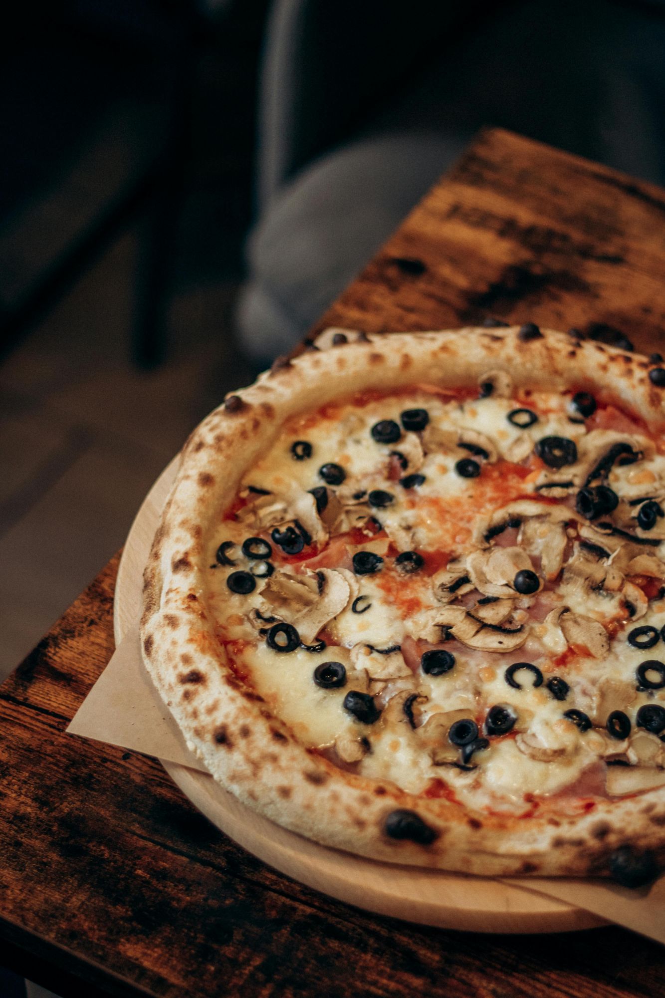 Pizza z oliwkami i pieczarkami na drewnianej desce na rustykalnym stole.