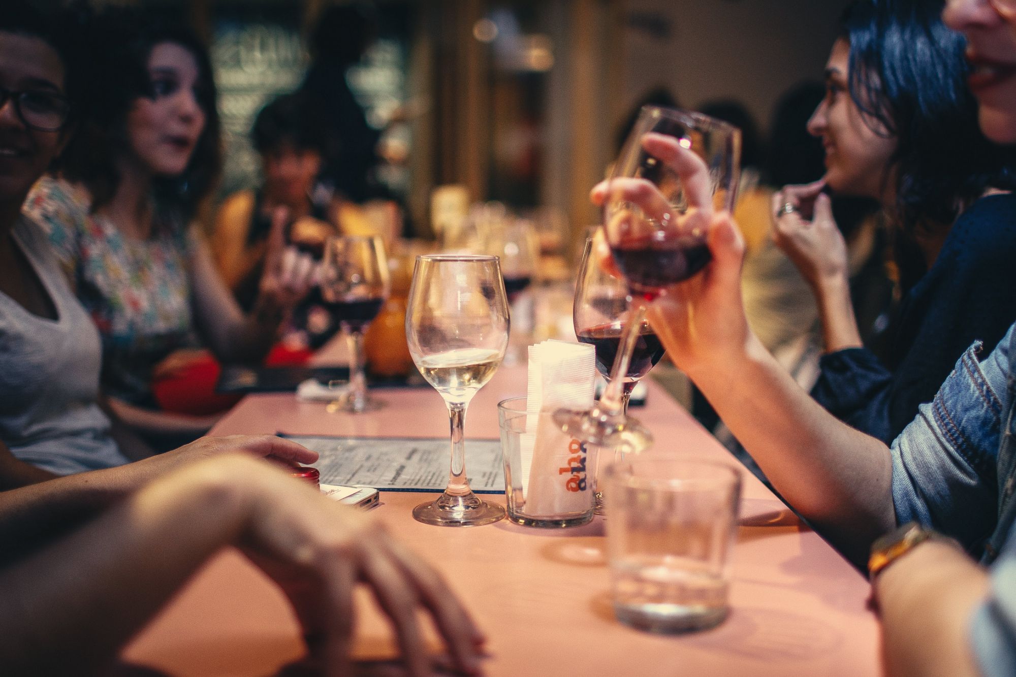 Kobiety przy stole, rozmawiające i pijące wino, przytulna restauracja z ciepłym oświetleniem.