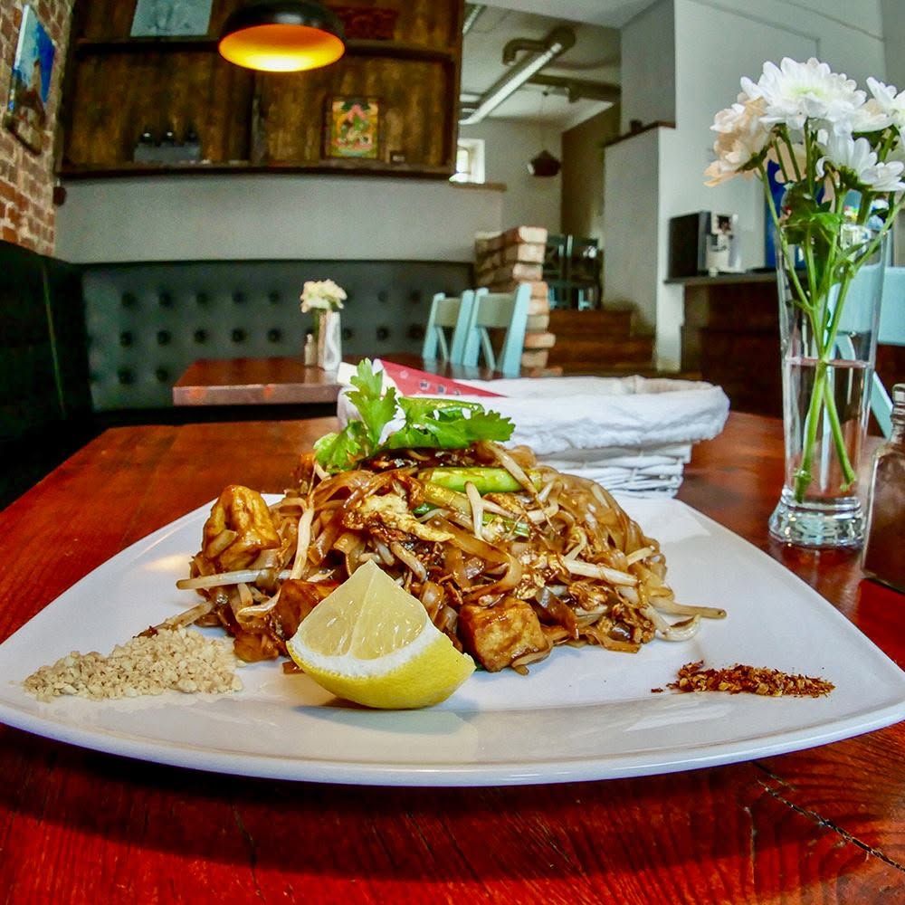 Talerz z azjatyckim daniem z makaronem, kurczakiem, limonką i posypką na drewnianym stole w restauracji.
