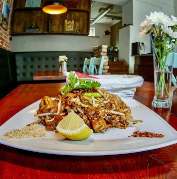 Talerz z azjatyckim daniem z makaronem, kurczakiem, limonką i posypką na drewnianym stole w restauracji.