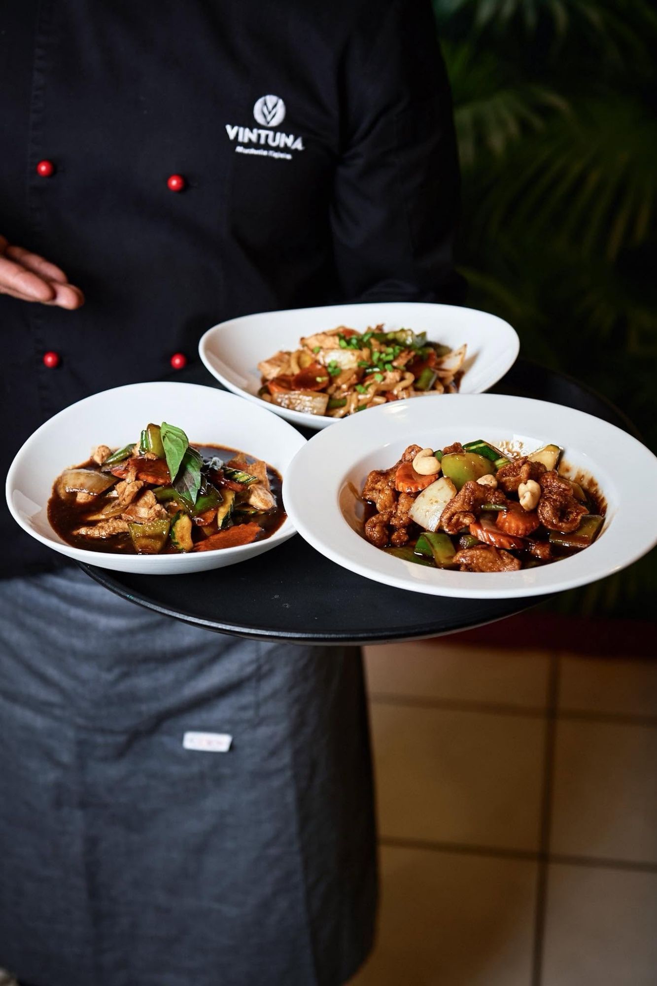 Szef kuchni serwuje trzy talerze potraw azjatyckich na czarnym półmisku w restauracji.