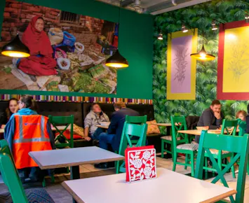 Uśmiechnięty kucharz trzyma organizery w restauracji z kolorowym wystrojem i zielonymi krzesłami.