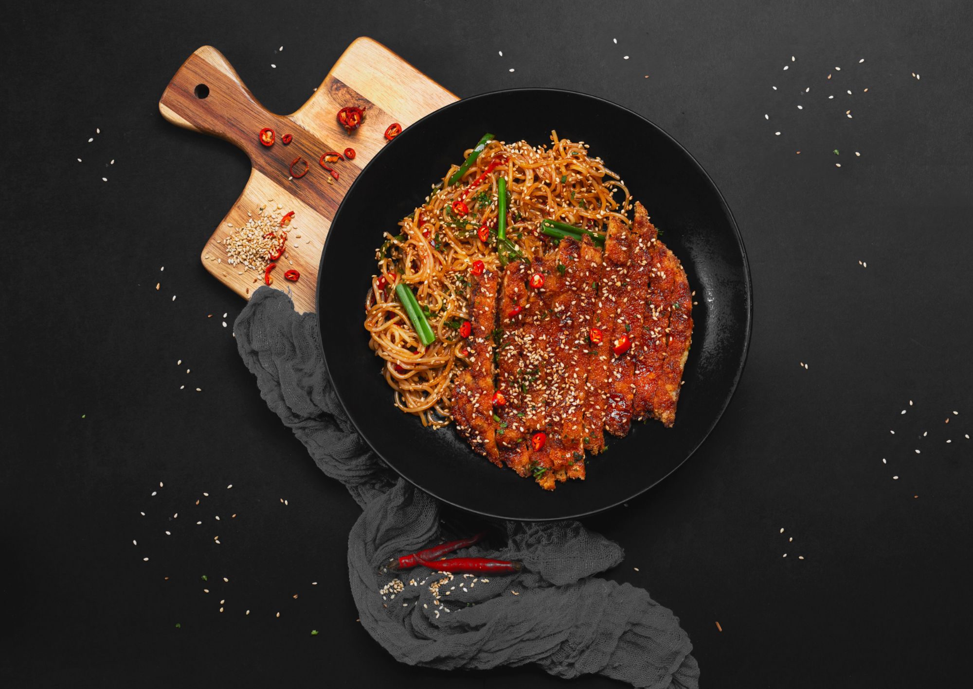 Makaron z sosem, chili, sezamem i warzywami podany na czarnym tle.