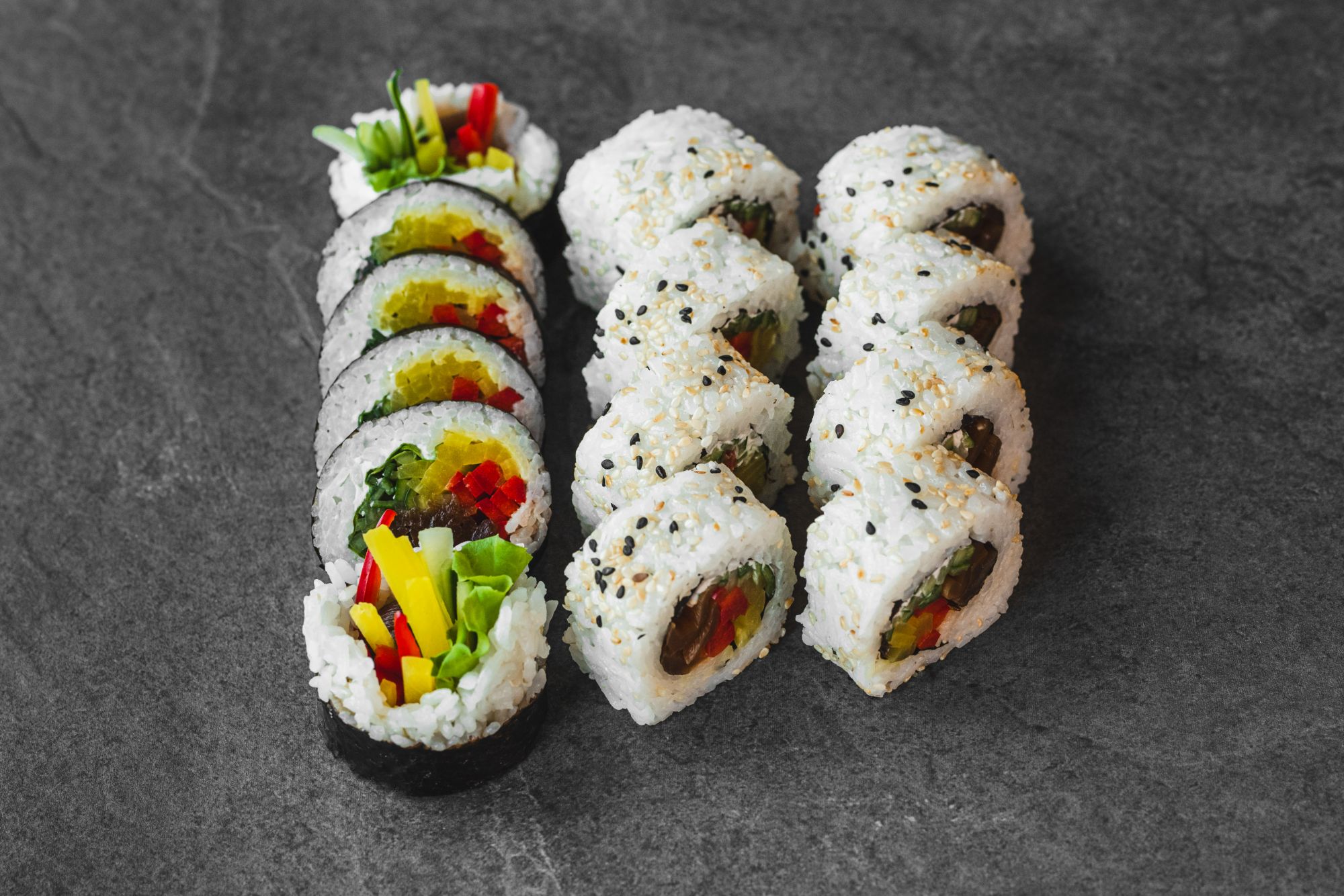 Zestaw sushi składający się z kształtnych rolek z warzywami na ciemnym tle.