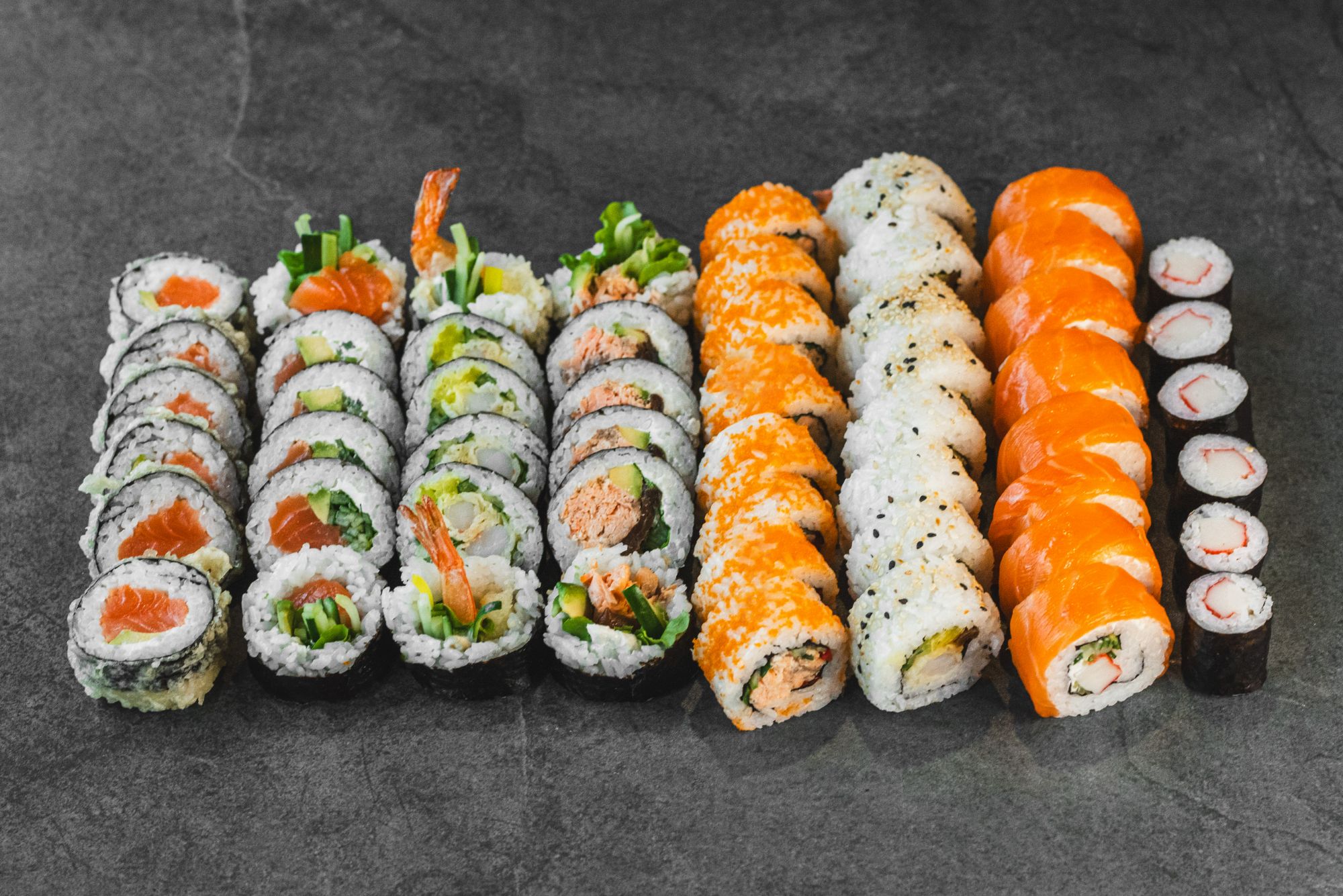 Układ różnych rodzajów sushi, w tym nigiri i maki, na ciemnym tle.