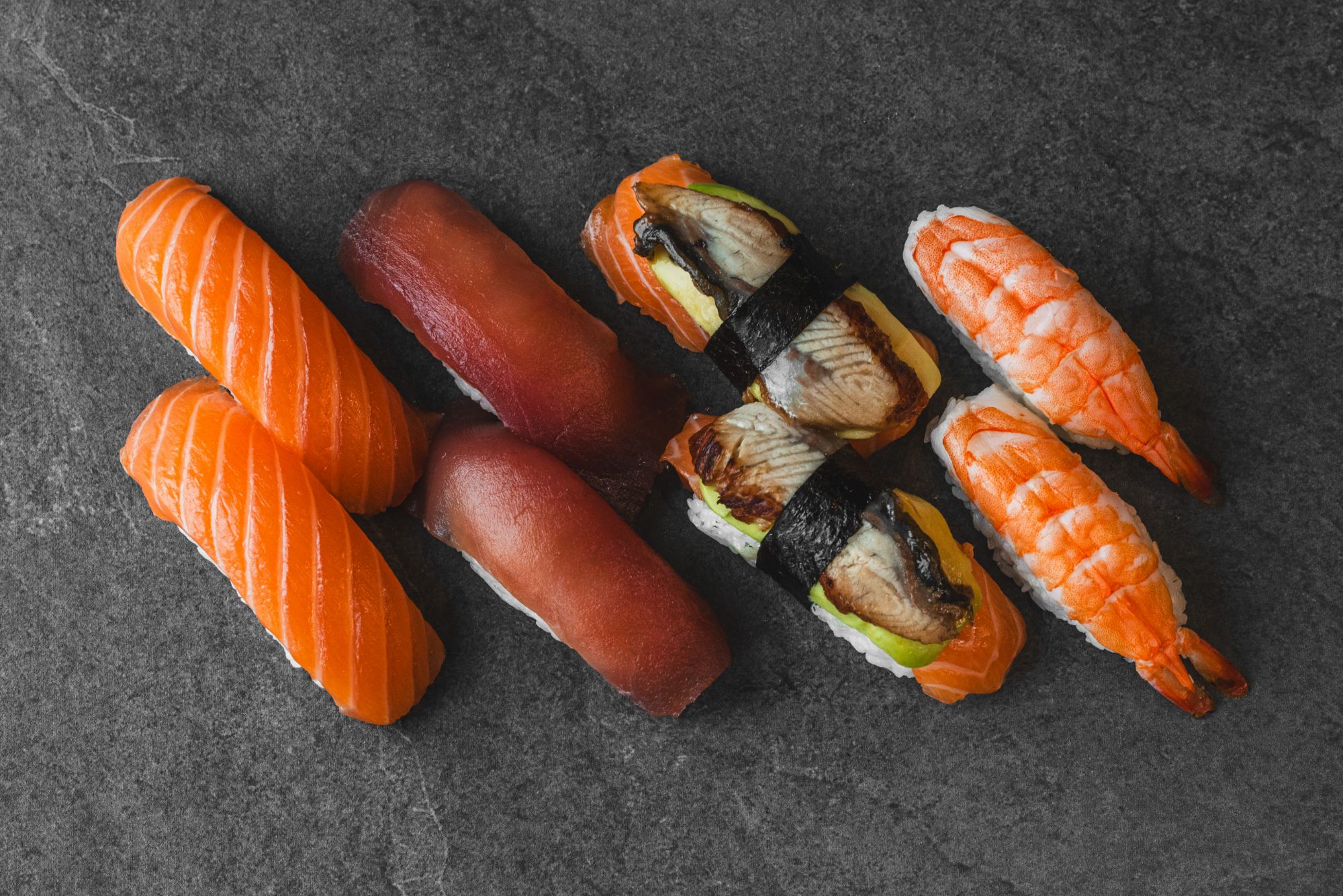 Sushi na czarnym tle: łosoś, tuńczyk, unagi i krewetki, podane w różnych formach i kolorach.