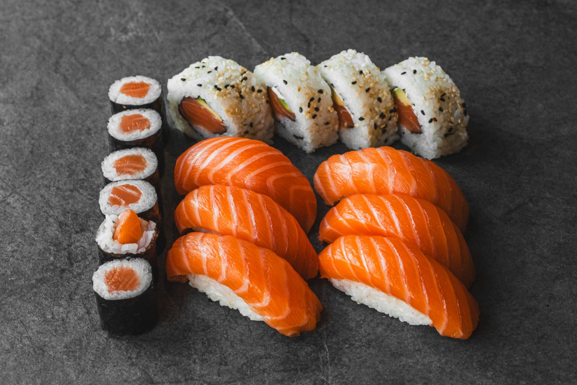 Sushi z łososiem - nigiri, rolki i maki na ciemnym tle.