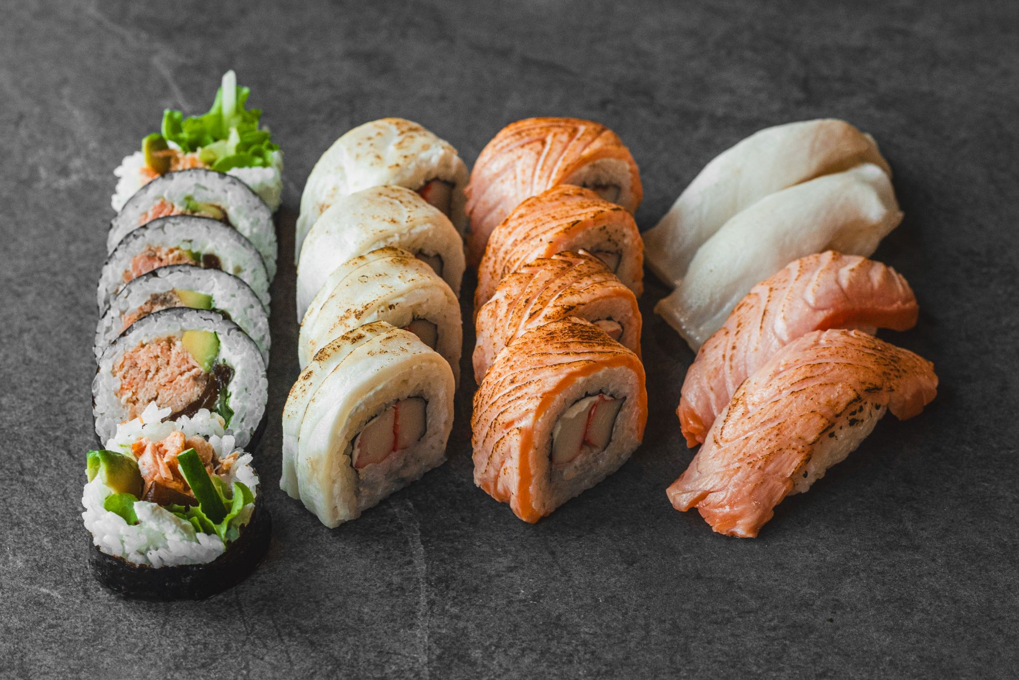Różnorodna porcja sushi, w tym sushi rolki, nigiri i sashimi na ciemnym tle.