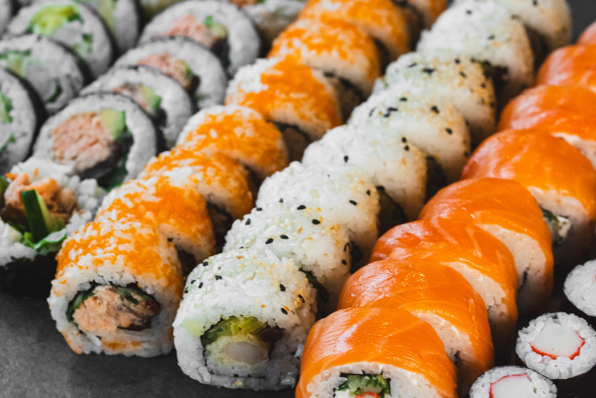 Różnorodne rolki sushi, w tym rolki z łososiem, tuńczykiem i warzywami, ułożone w estetyczny sposób.