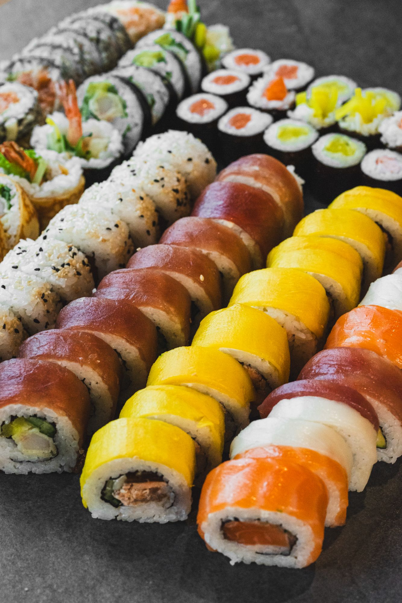 Różnorodne rolki sushi w różnych kolorach na ciemnym tle, w tym klasyczne nigiri i futomaki.