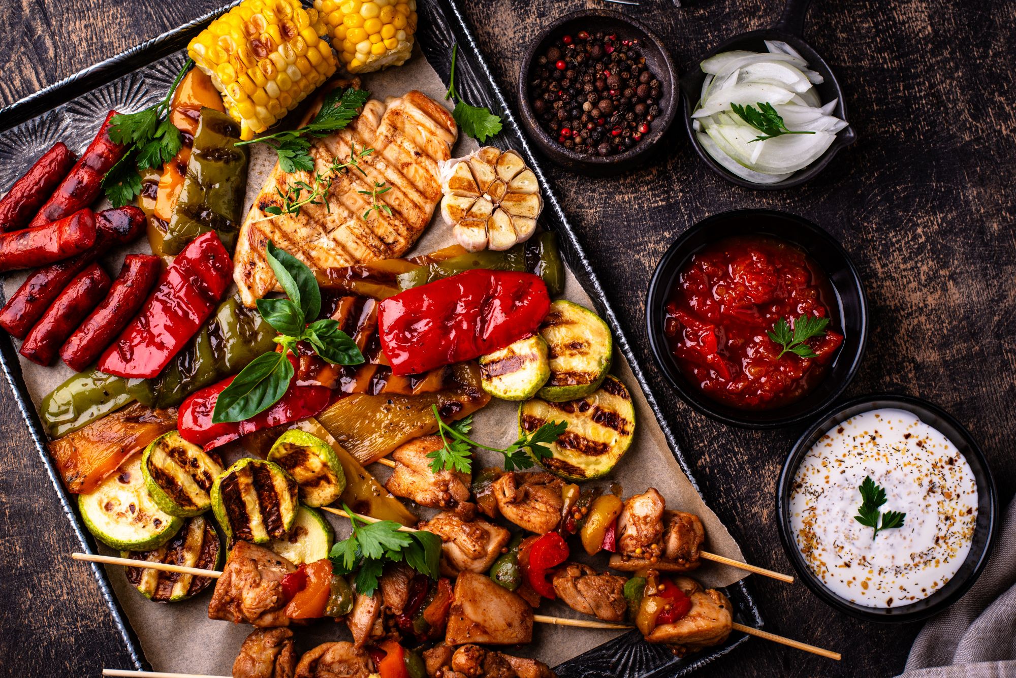 Talerz z grillowanym mięsem, warzywami, kukurydzą, sosami i przyprawami, dekorowany świeżą kolendrą.