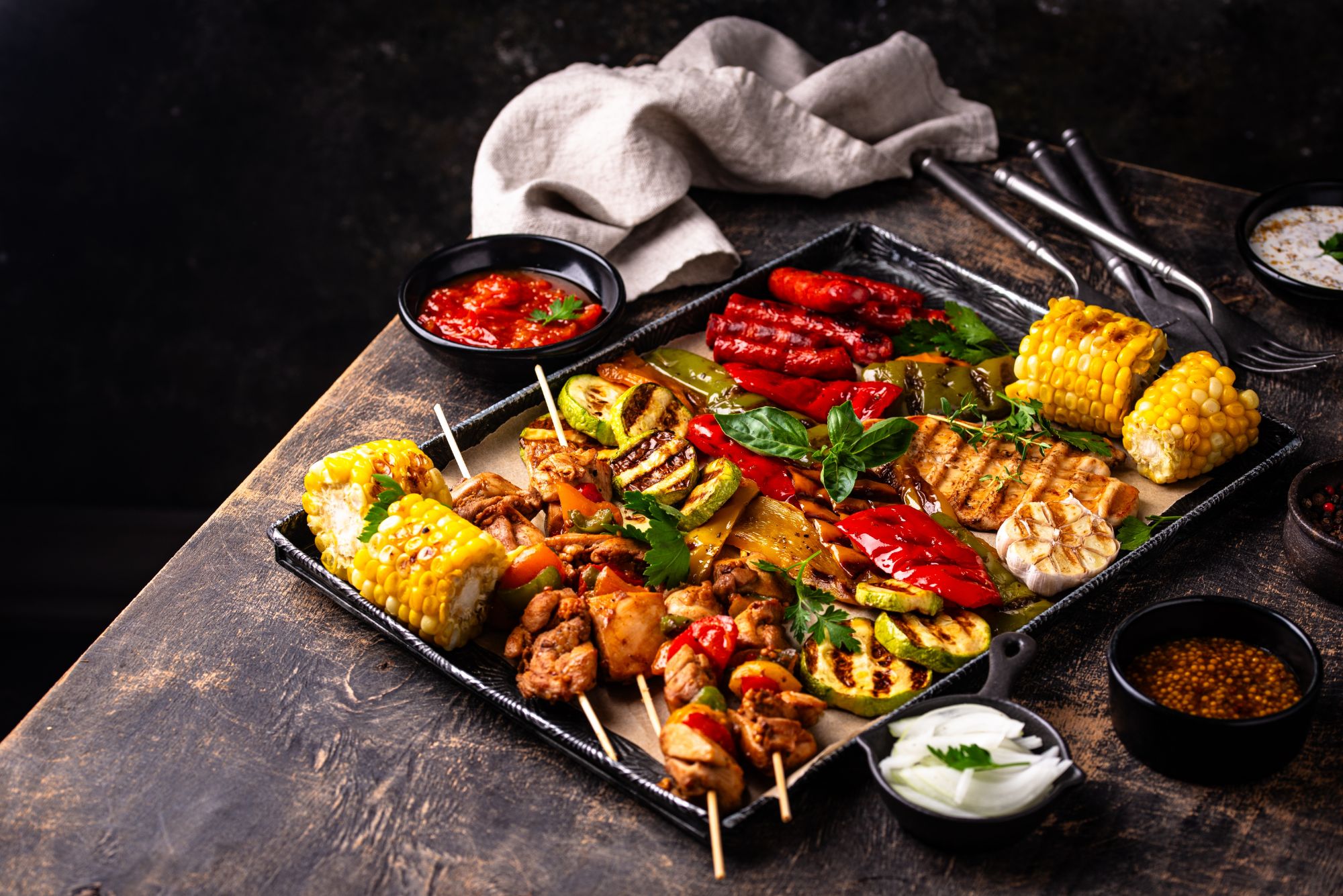 Grillowane mięso, warzywa, szaszłyki i sosy na tacy, idealne dla miłośników kuchni barbecue.