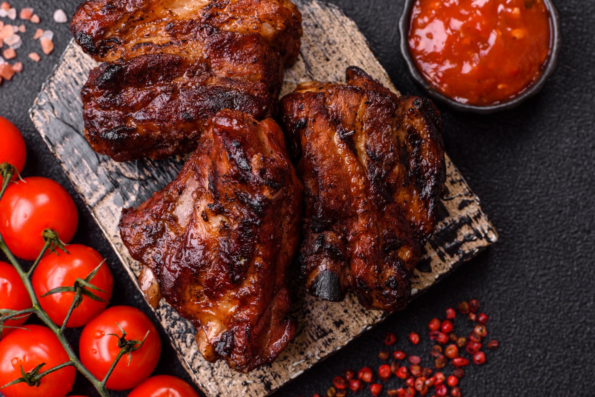 Grillowane żeberka wieprzowe na talerzu z pomidorami i sosem BBQ.