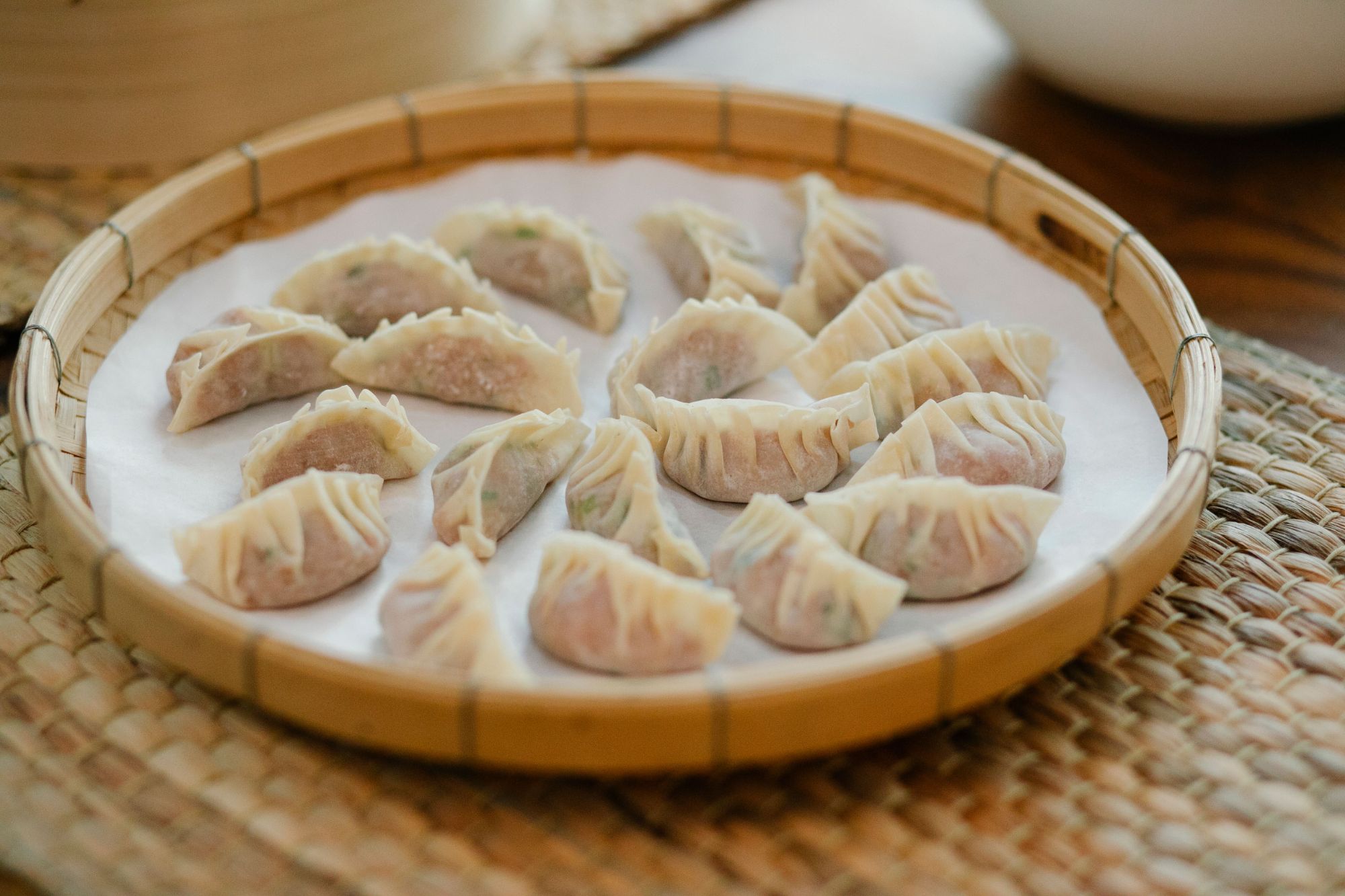 Dumplings ułożone na bambusowym talerzu, na tle plecionej maty.
