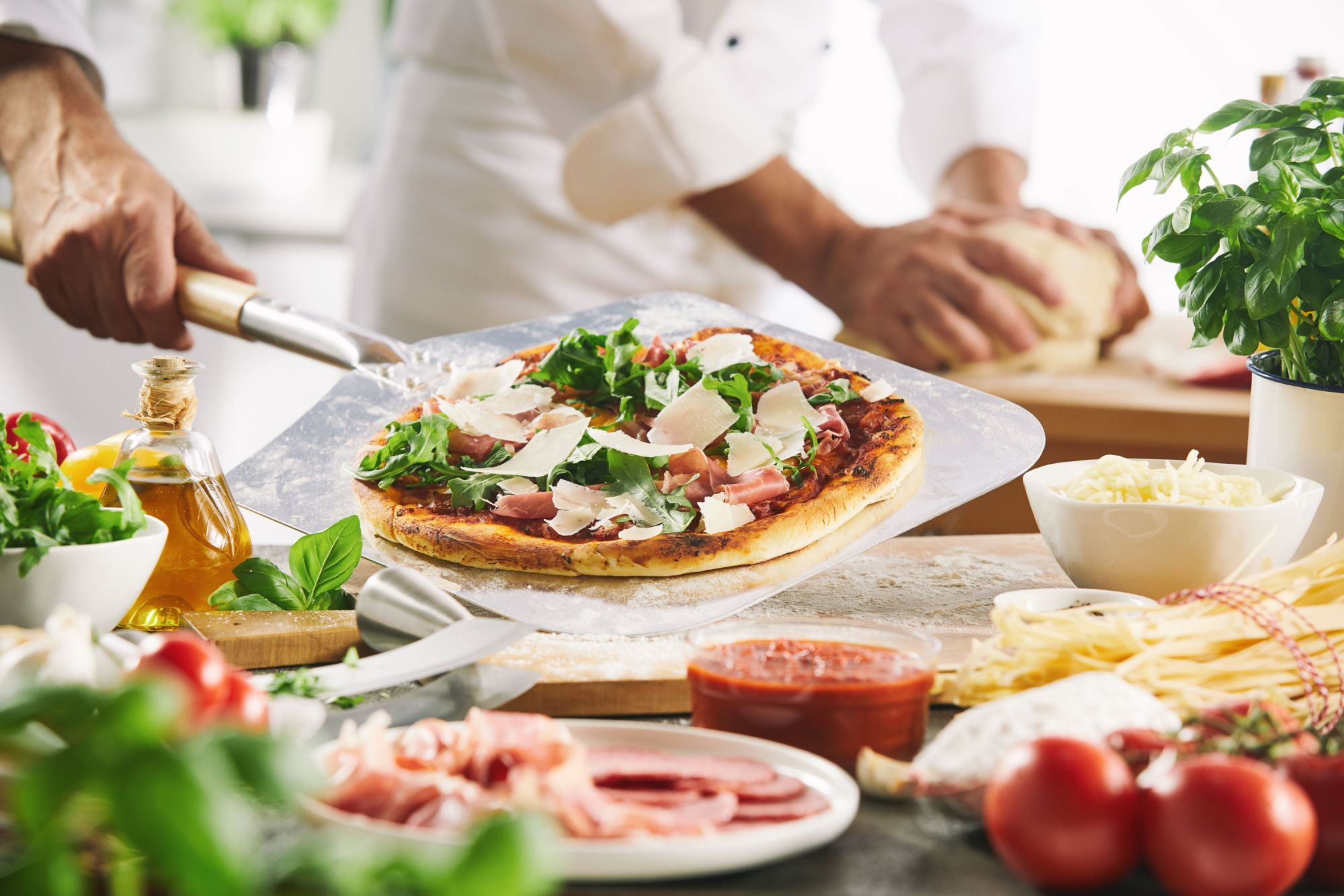 Pizze z rukolą, serem i wędliną, przygotowywane w kuchni przez kucharza.
