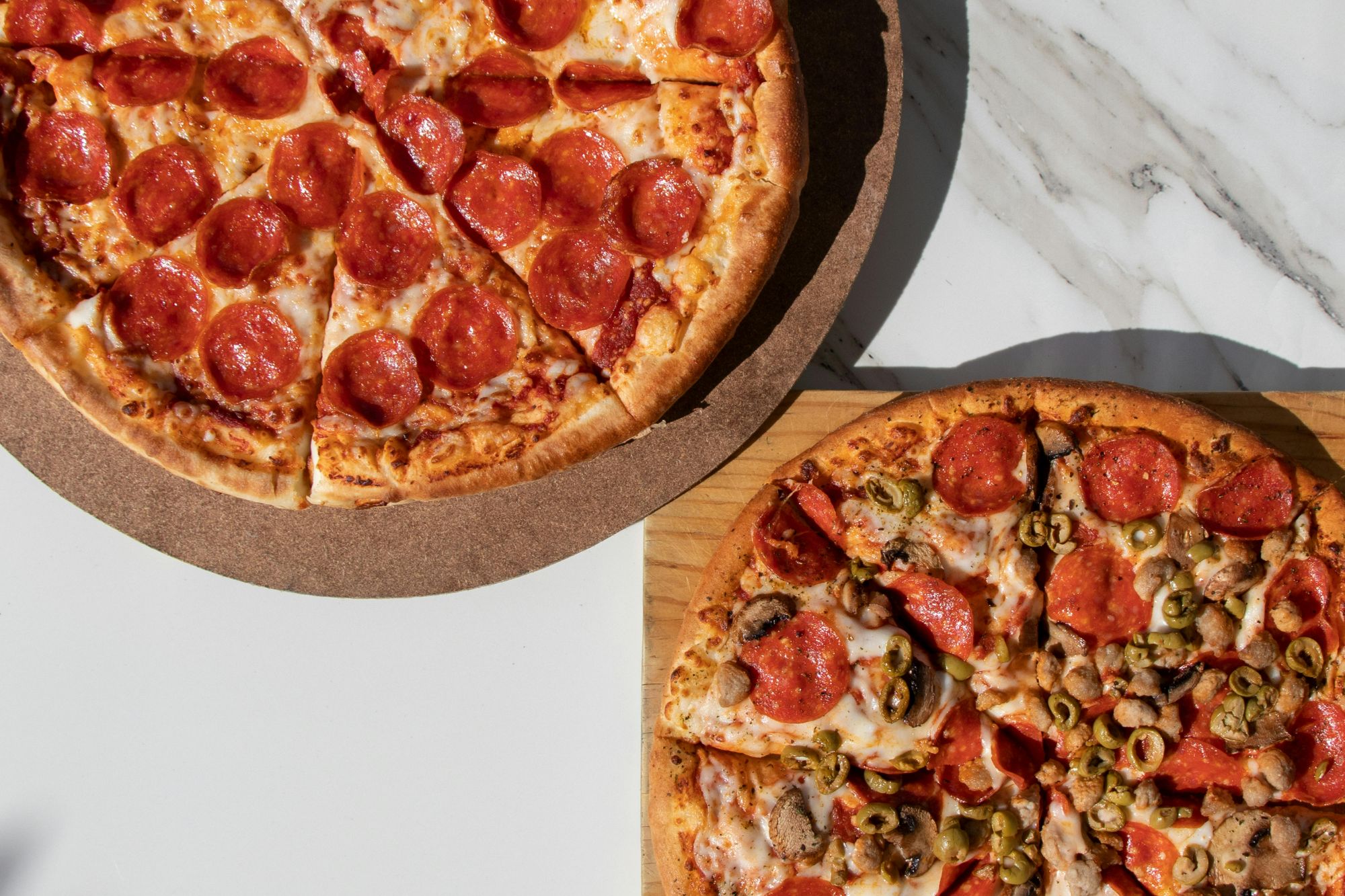 Dwie pizze na stole: jedna z pepperoni, druga z pepperoni, oliwkami i pieczonym kurczakiem.