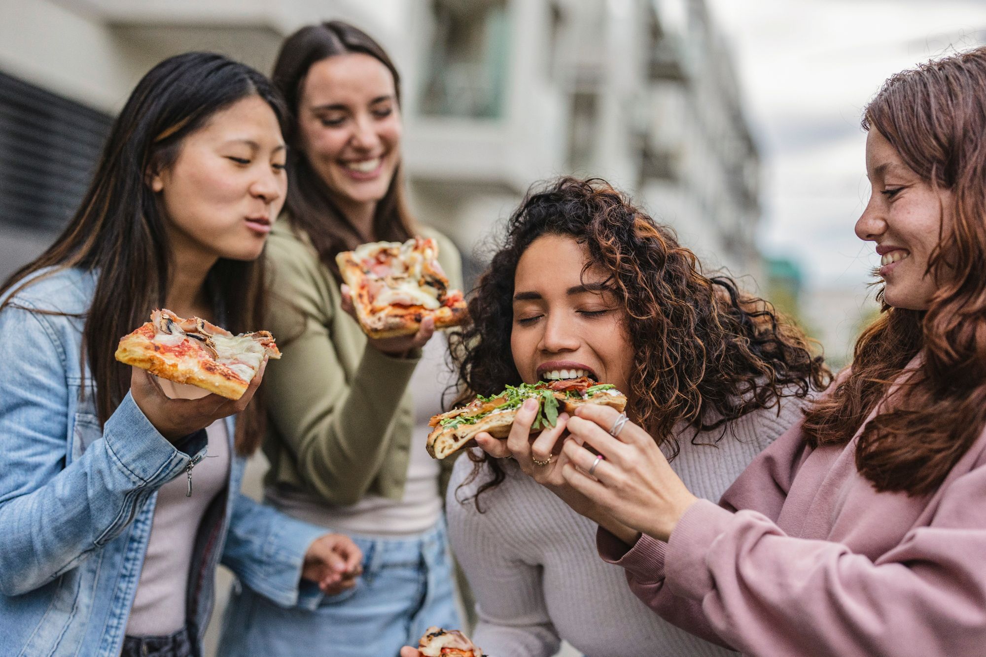 Cztery kobiety bawią się razem, jedząc pizzę na świeżym powietrzu, uśmiechając się do siebie.