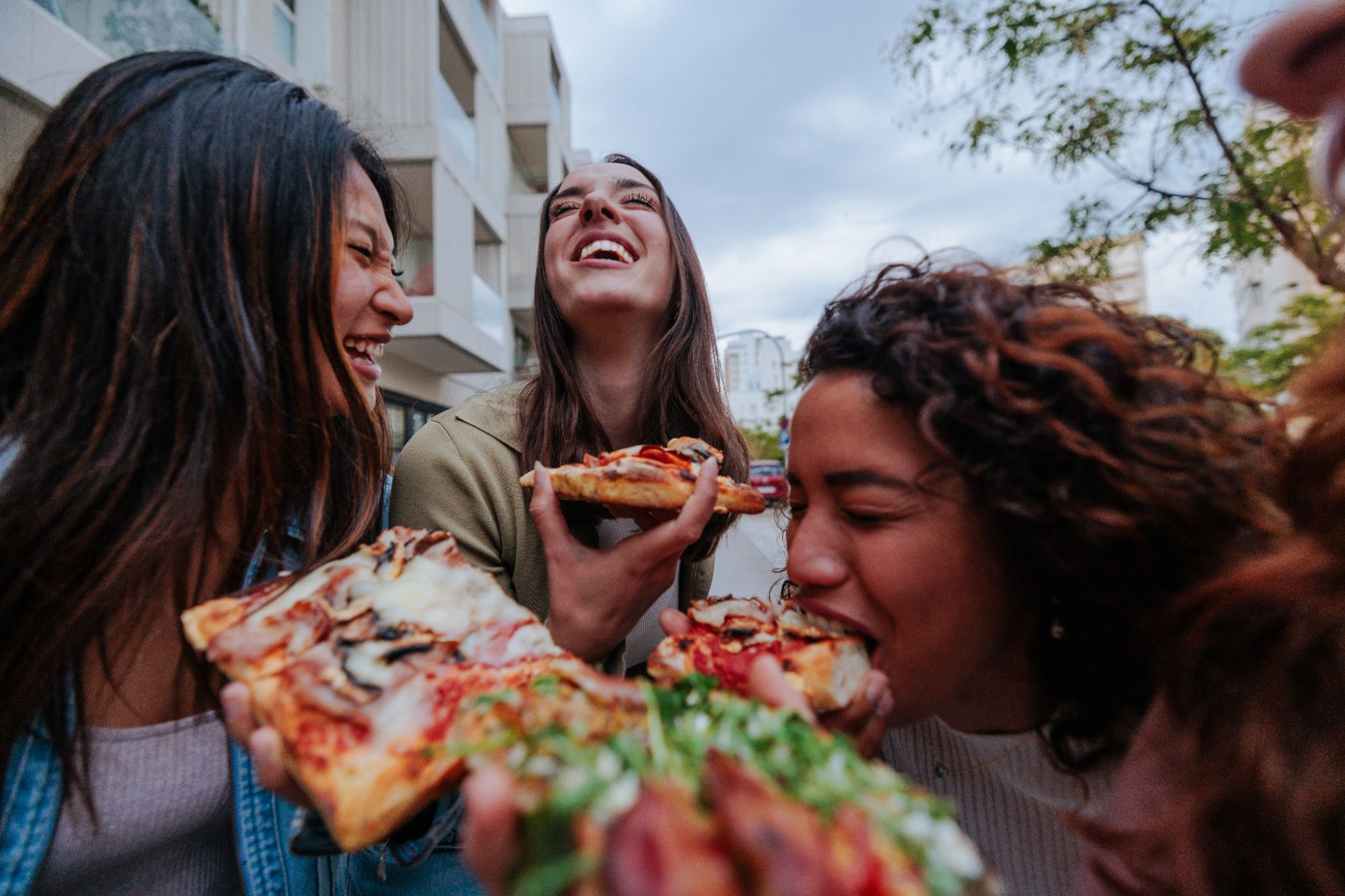 Grupa kobiet bawi się, jedząc pizzę na świeżym powietrzu, śmiejąc się i dzieląc chwilą radości.