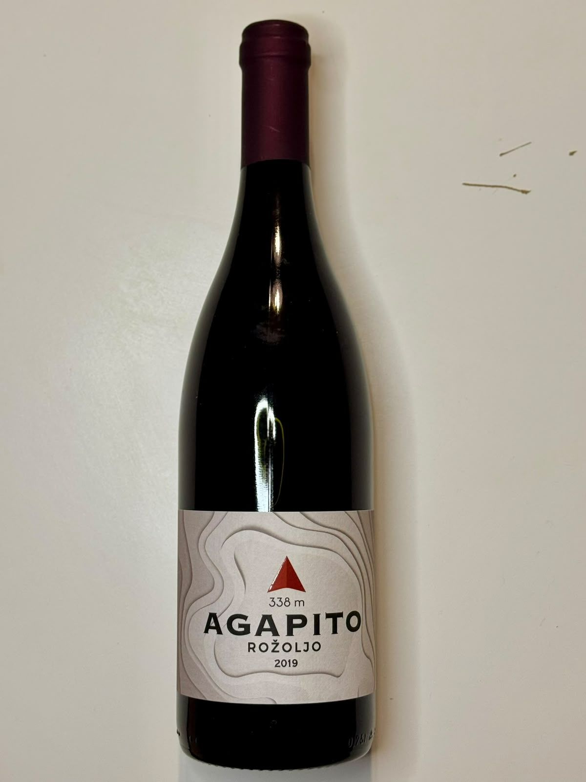 Boca crvenog vina Agapito Rožoljo 2019, s elegatnom etiketom i ljubičastim čepom.