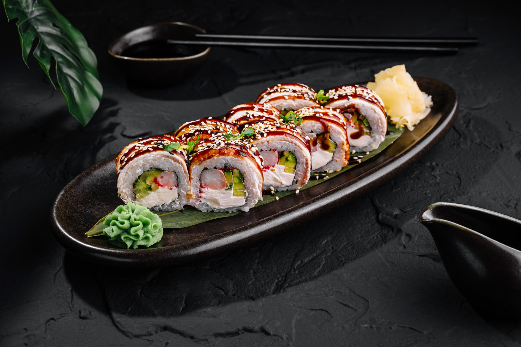 Sushi na czarnej tacy, z różnymi składnikami, posypane sezamem i podane z wasabi i imbirem.